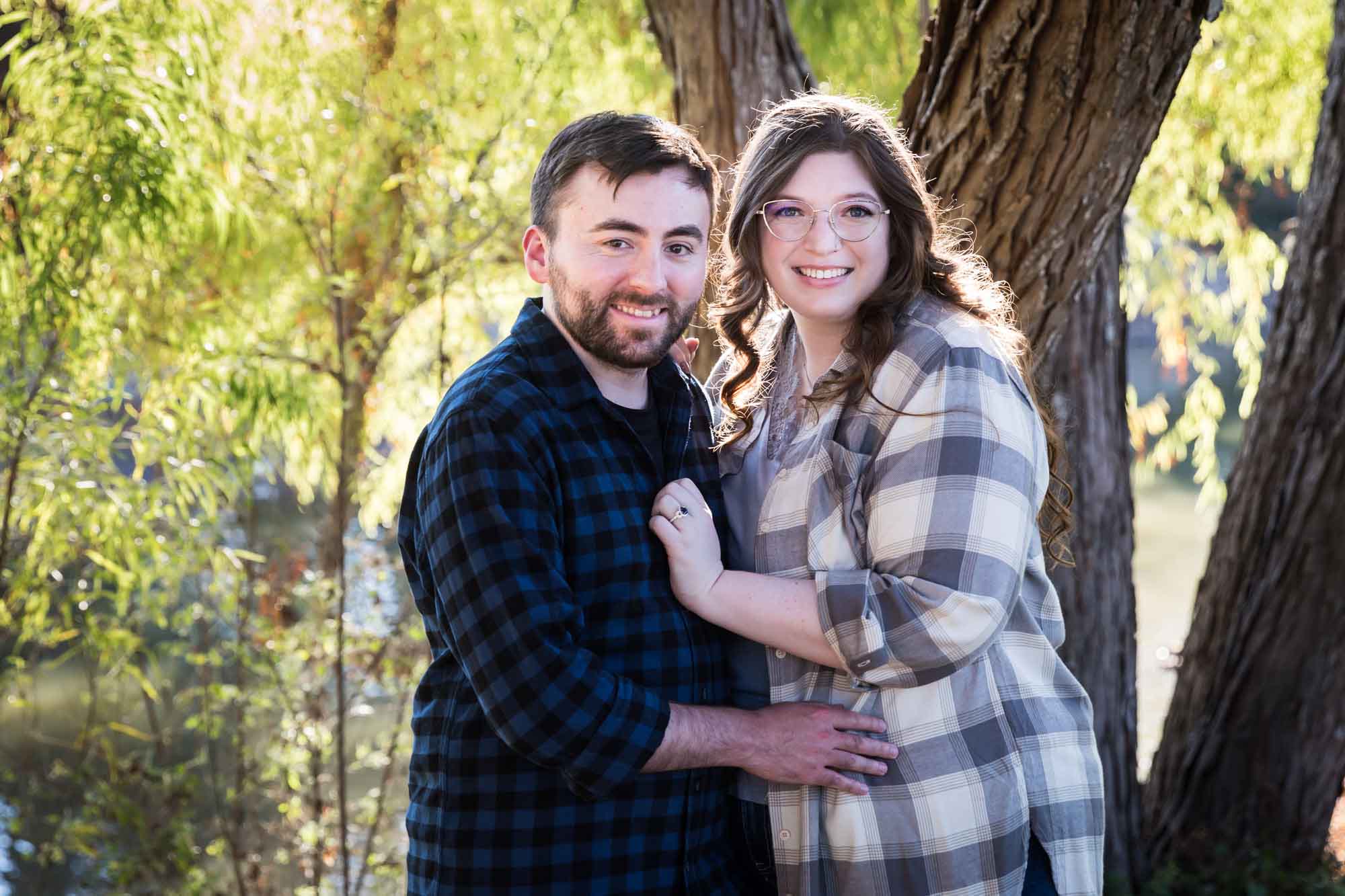 Boerne engagement photos of couple wearing plaid shirts hugging in front of trees in River Road Park