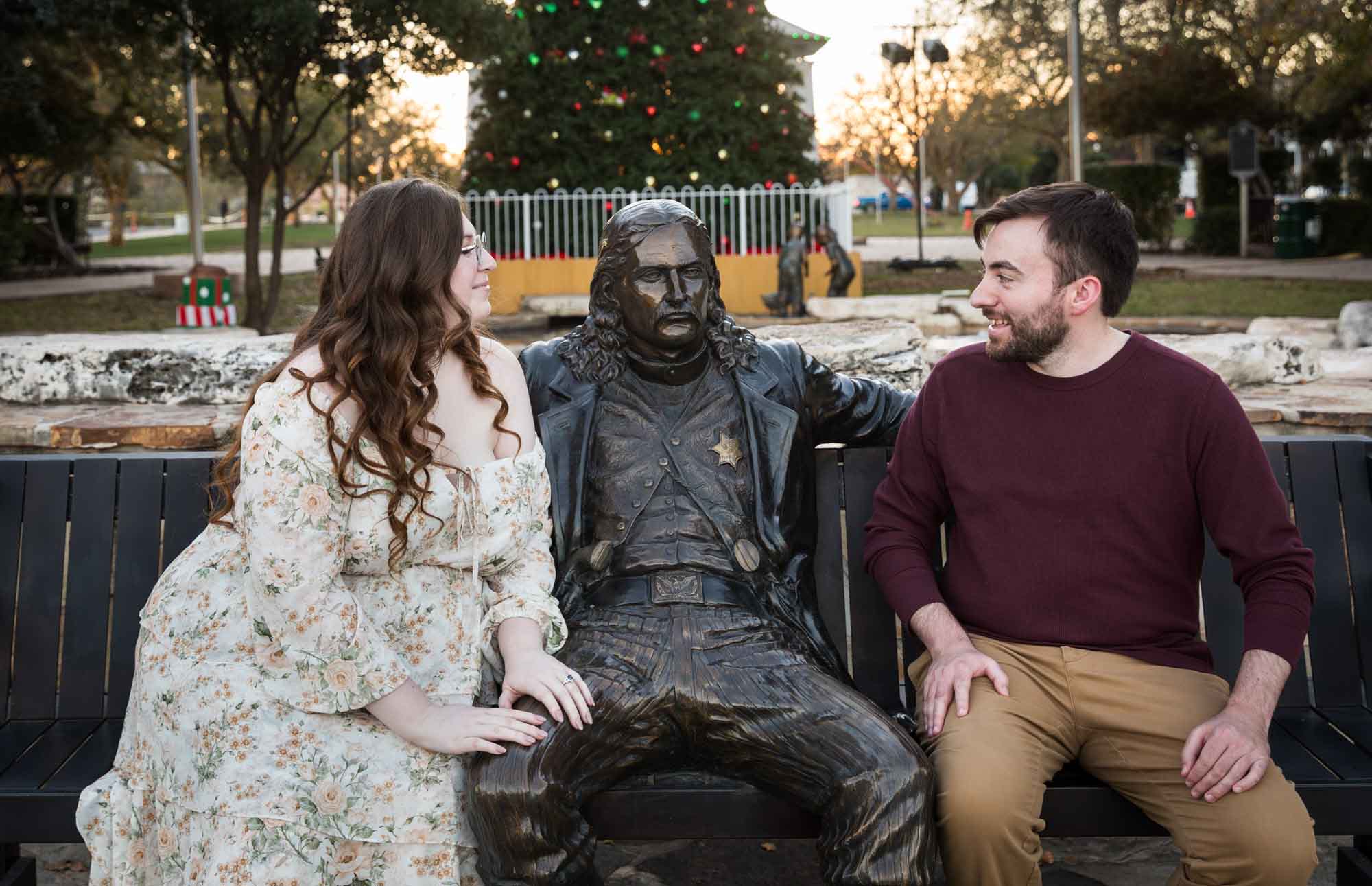 Boerne engagement photos of woman and man sitting beside statue of Wild Bill Hickok in Main Plaza