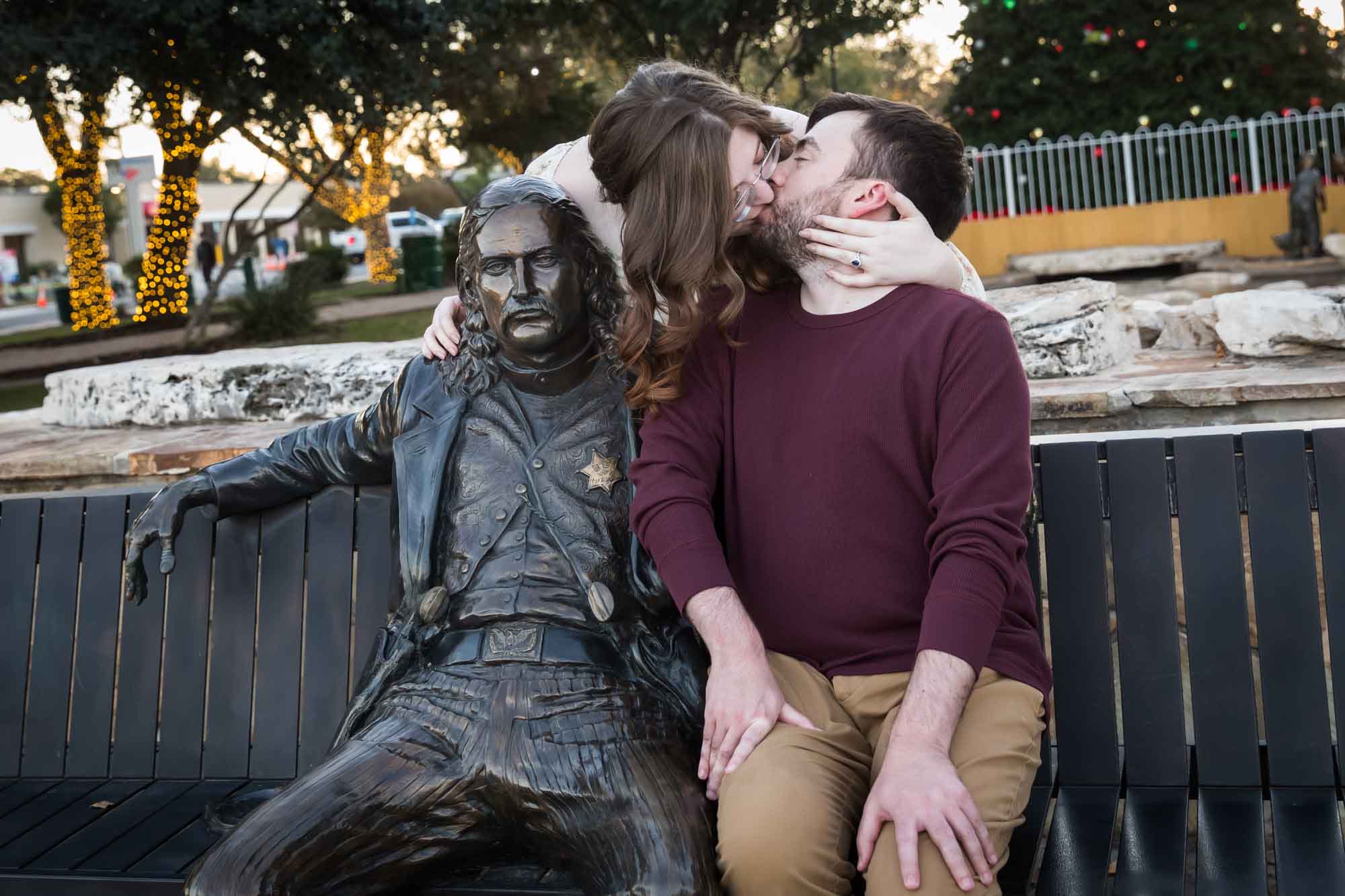 Boerne engagement photos of woman and man kissing beside statue of Wild Bill Hickok in Main Plaza