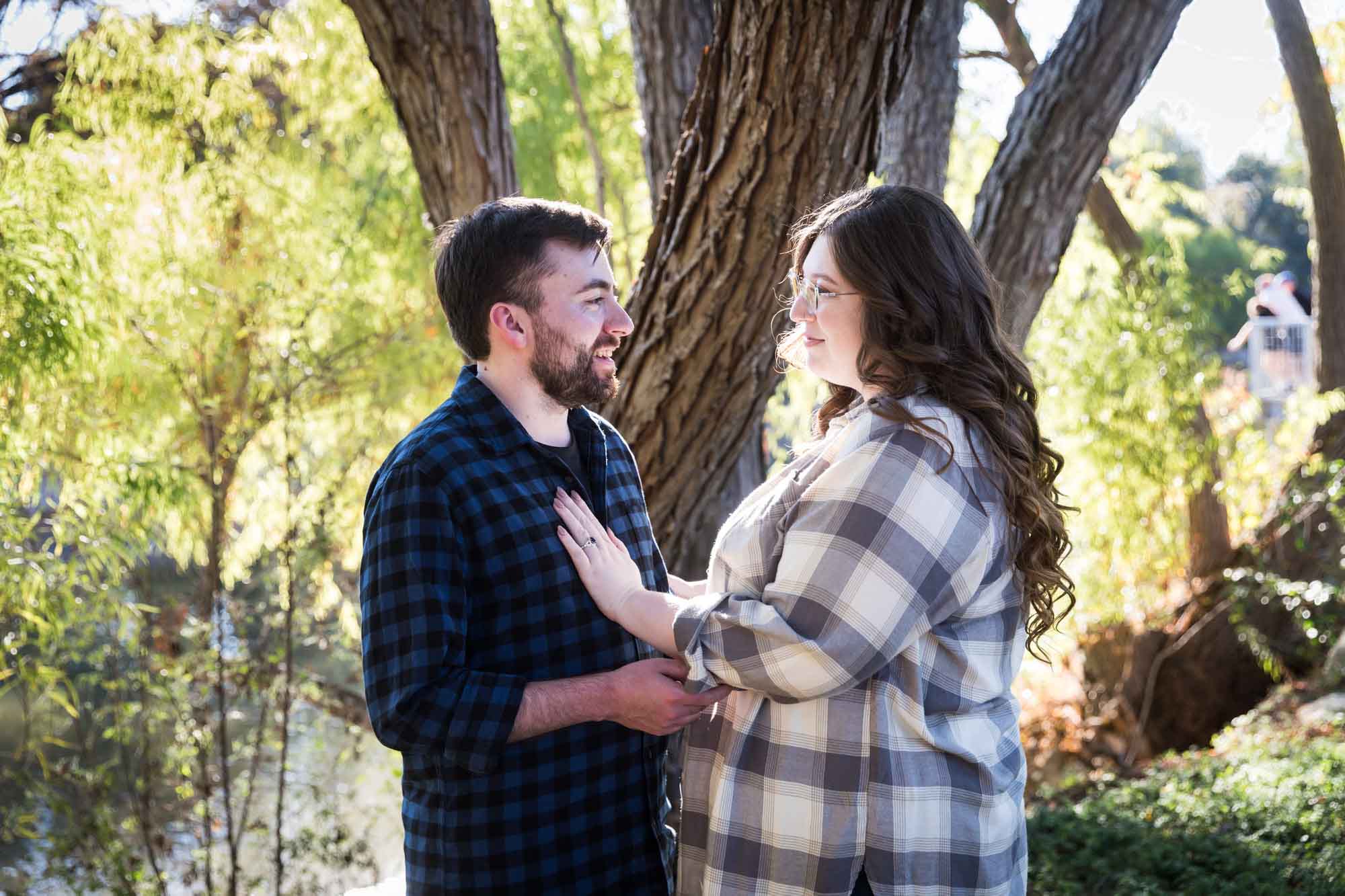 Boerne engagement photos of couple wearing plaid shirts hugging in front of trees in River Road Park