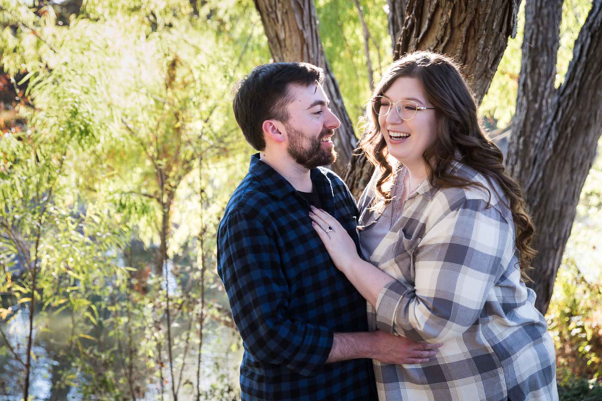 Boerne engagement photos of couple wearing plaid shirts hugging in front of trees in River Road Park