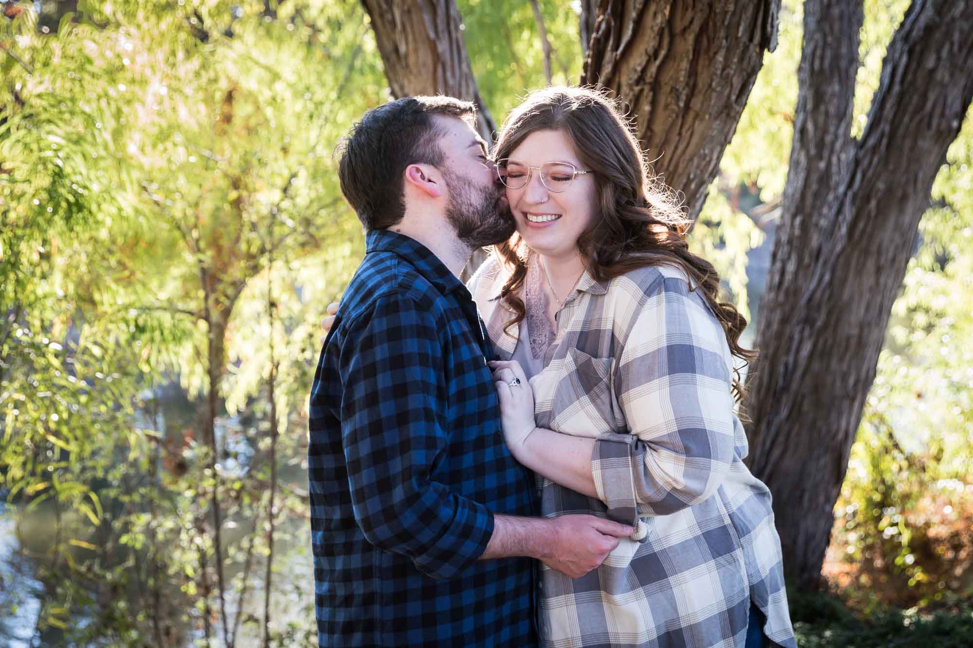Boerne engagement photos of couple wearing plaid shirts kissing in front of trees in River Road Park