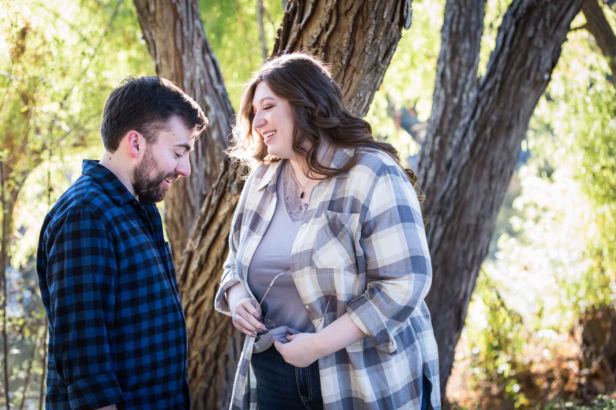 Boerne engagement photos of couple wearing plaid shirts laughing in front of trees in River Road Park