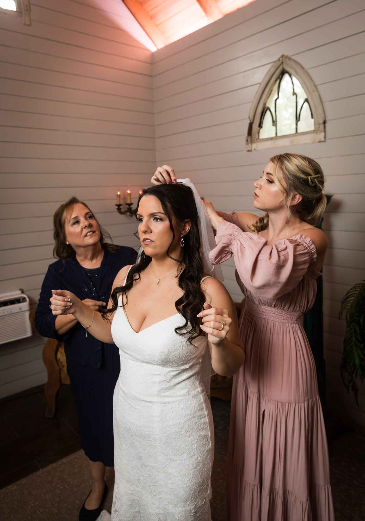 Mother and woman wearing pink dress helping to put veil in bride's hair in bridal suite at a Chapel Dulcinea wedding