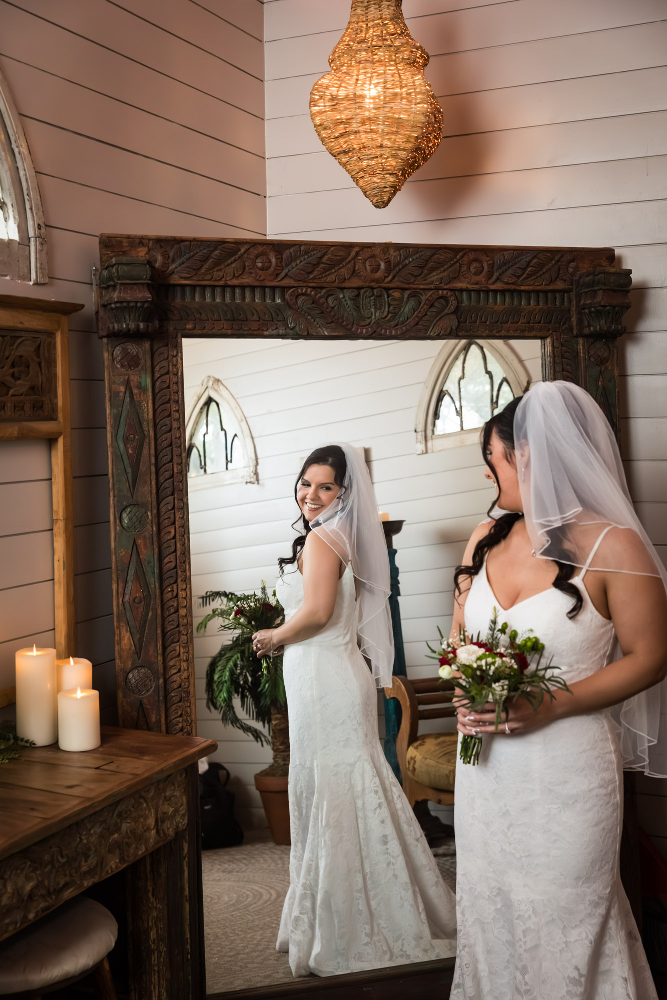 Bride wearing veil and holding bouquet looking at herself in the mirror in bridal suite at a Chapel Dulcinea wedding