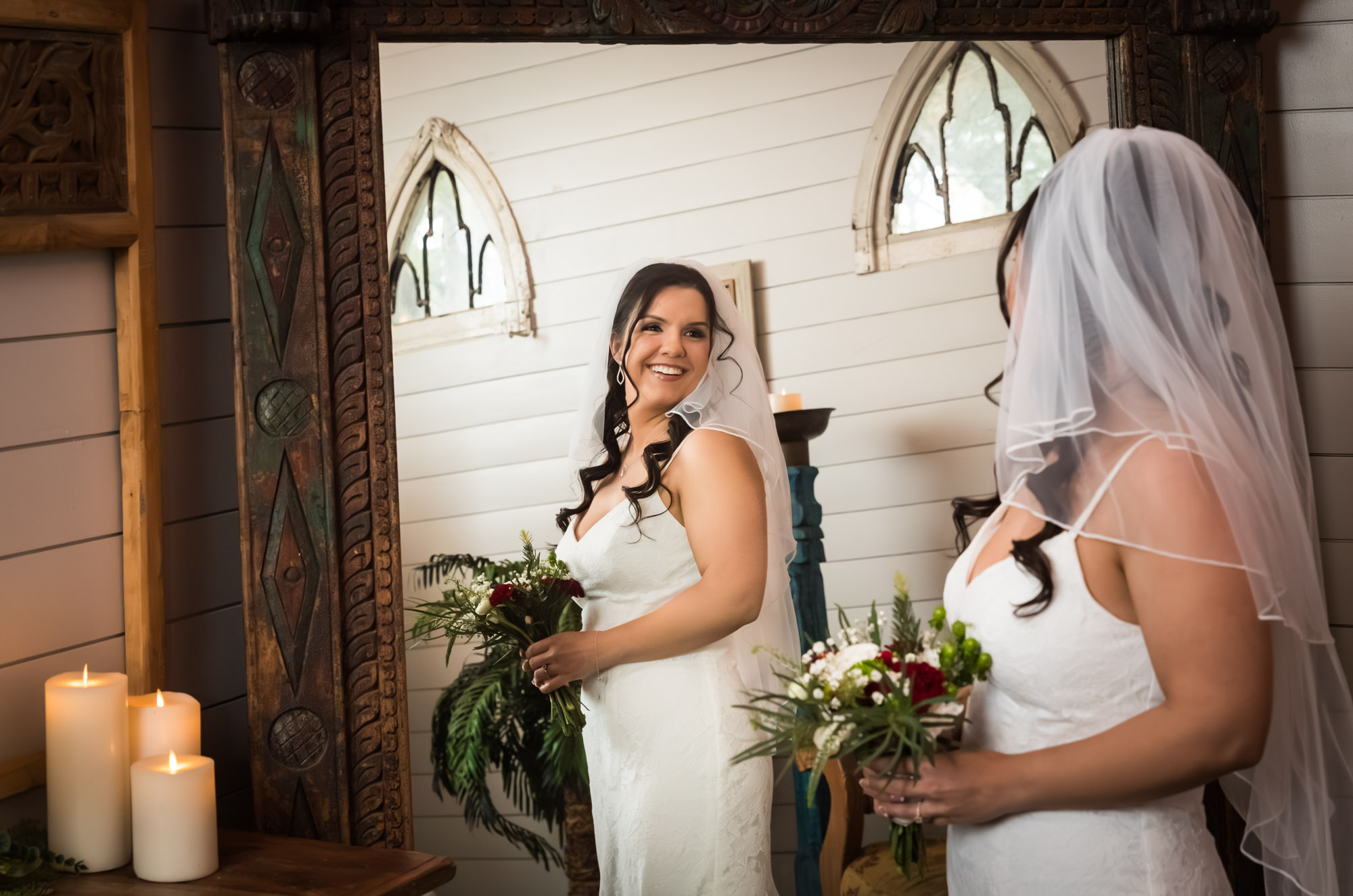 Bride wearing veil and holding bouquet looking at herself in the mirror in bridal suite at a Chapel Dulcinea wedding