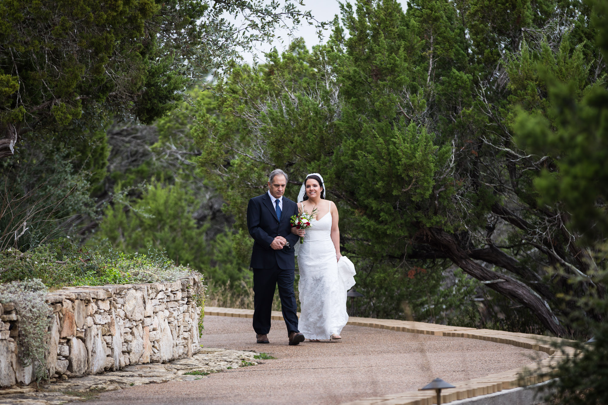 Father walking bride wearing sleeveless dress and veil down pathway during ceremony at a Chapel Dulcinea wedding