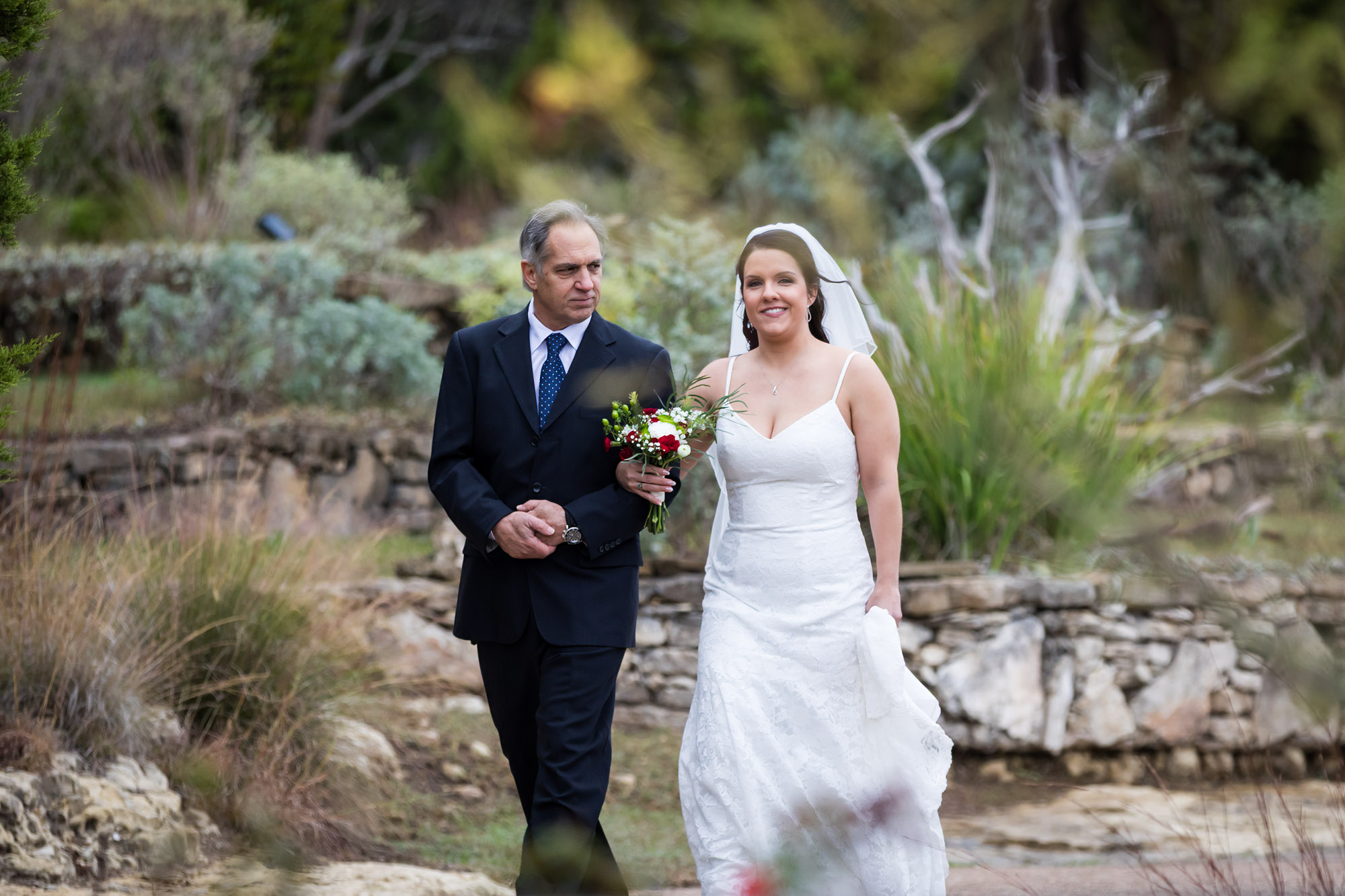 Father walking bride wearing sleeveless dress and veil down pathway during ceremony at a Chapel Dulcinea wedding