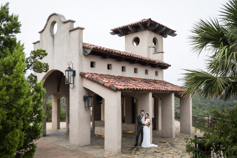 Bride wearing veil and groom standing by column beside chapel at a Chapel Dulcinea wedding