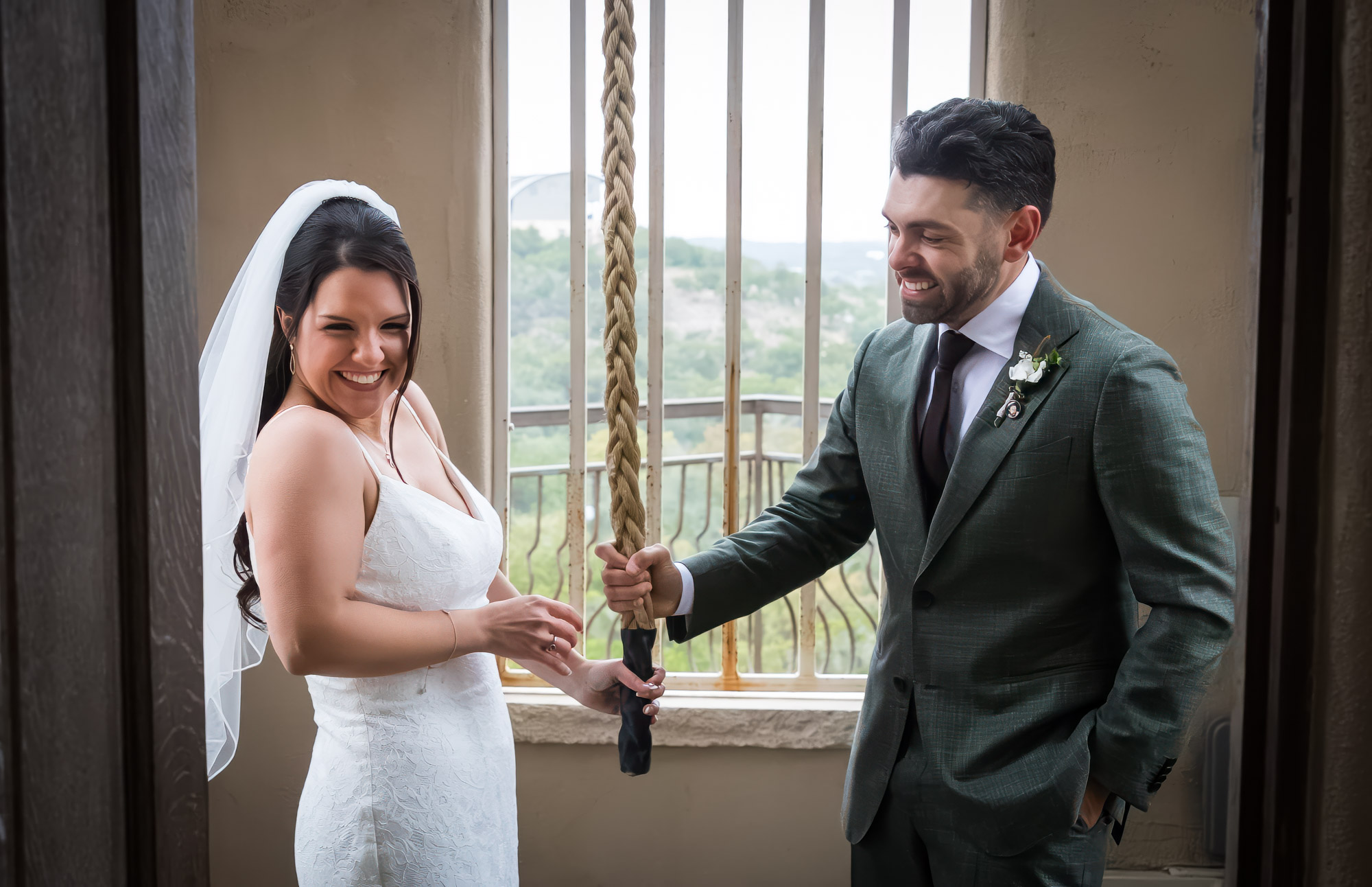 Bride wearing veil and groom ringing bell in room in front of window at a Chapel Dulcinea wedding