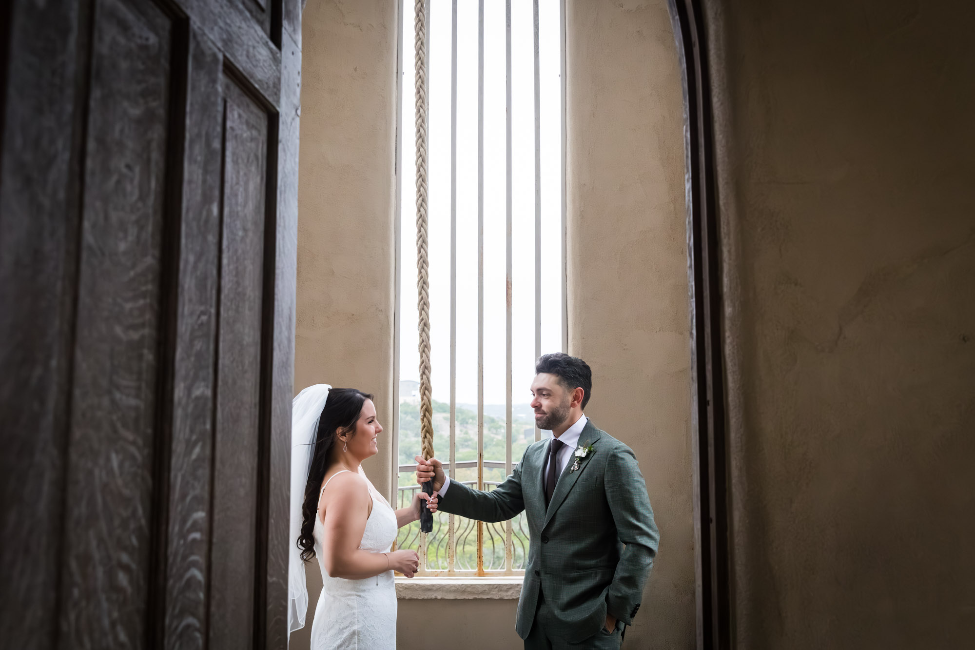 Bride wearing veil and groom ringing bell in room in front of window at a Chapel Dulcinea wedding