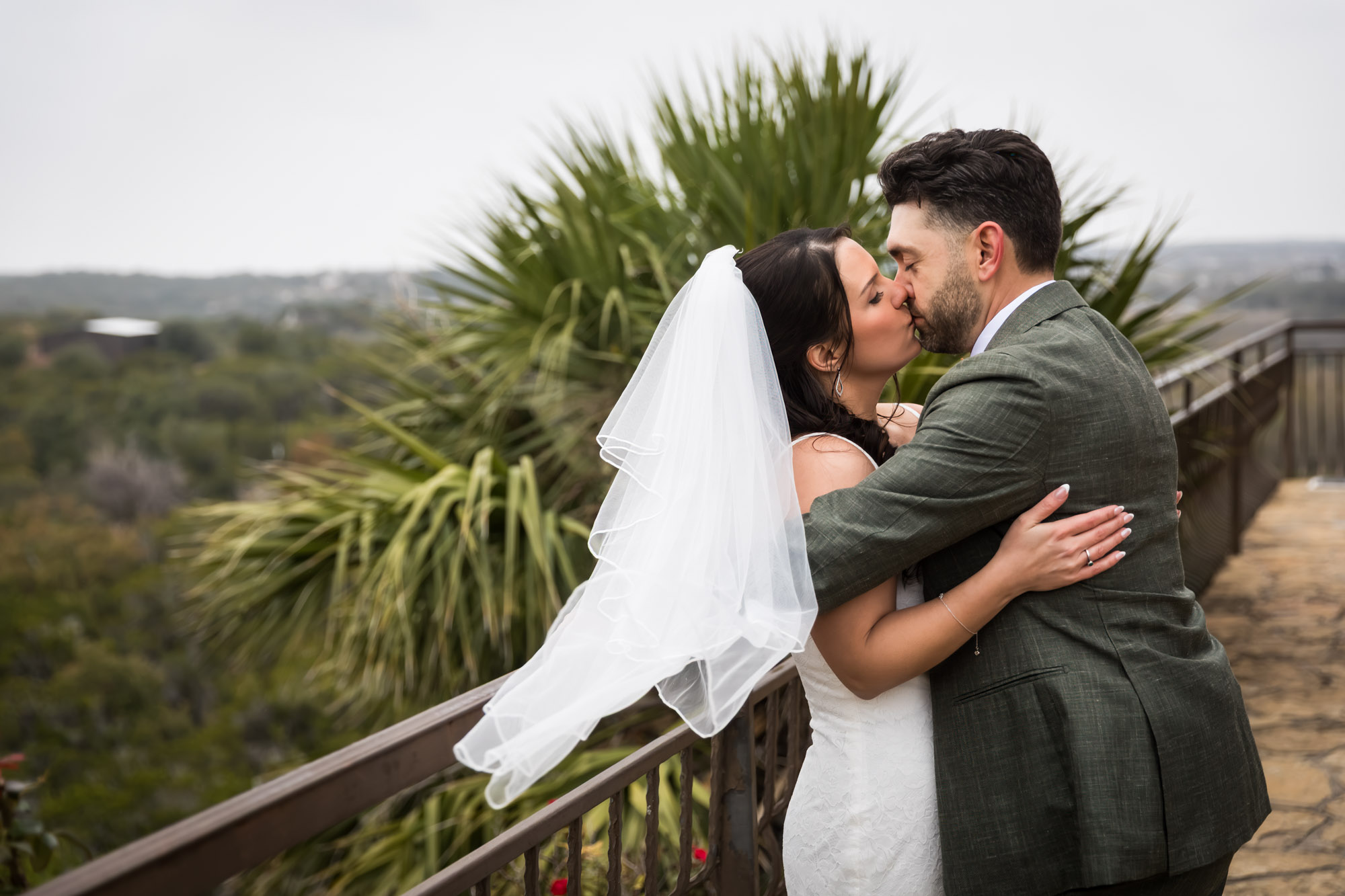 Bride wearing veil kissing groom against railing at a Chapel Dulcinea wedding