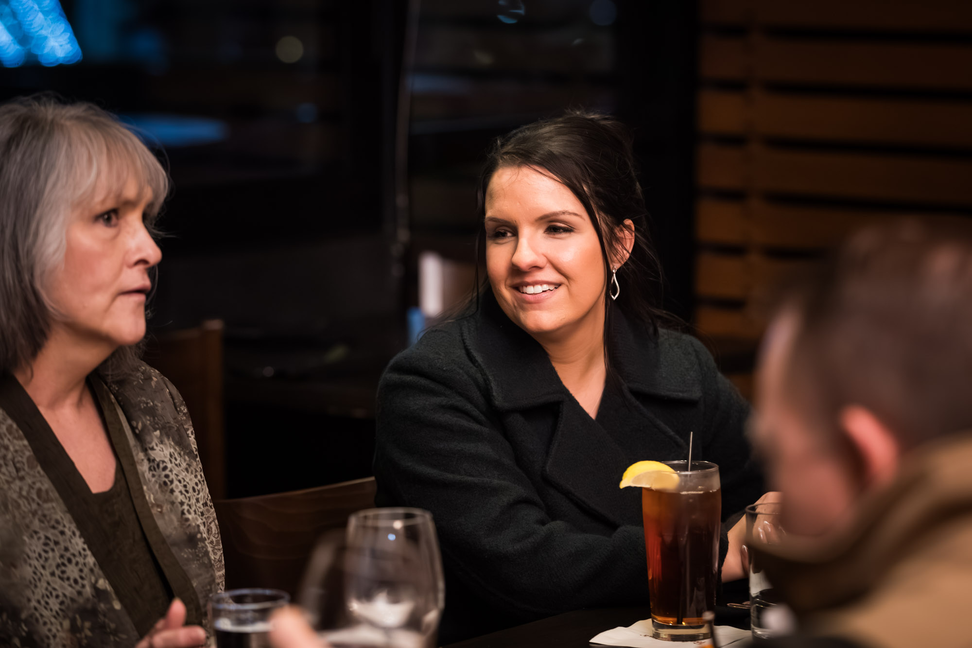 Woman with brown hair wearing black jacket seated at table during wedding reception