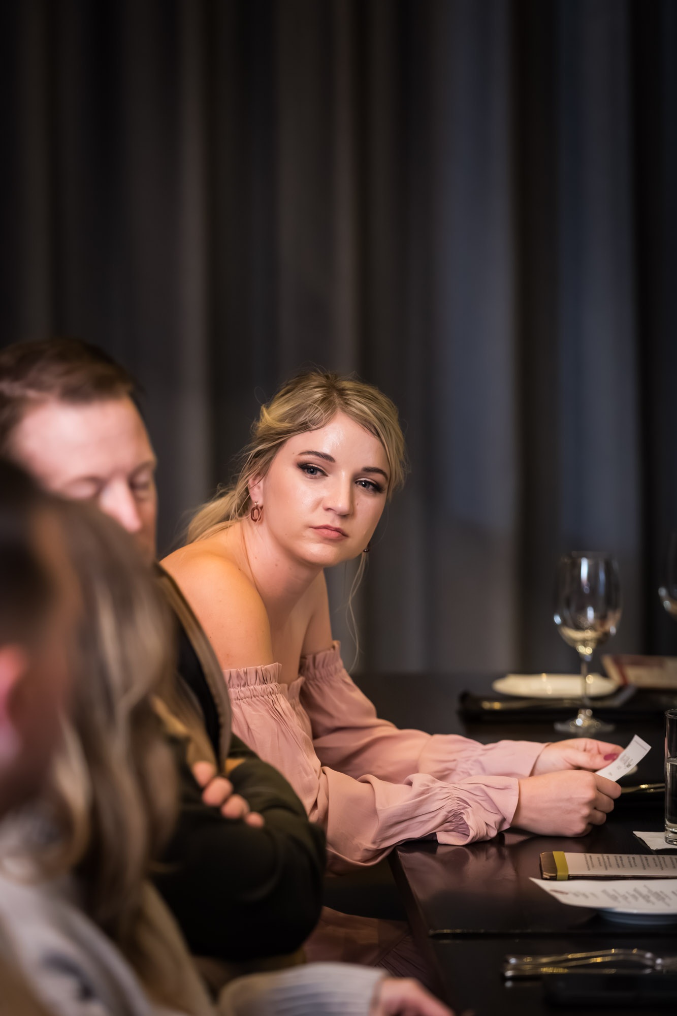 Woman with blonde hair wearing pink dress seated at table during wedding reception