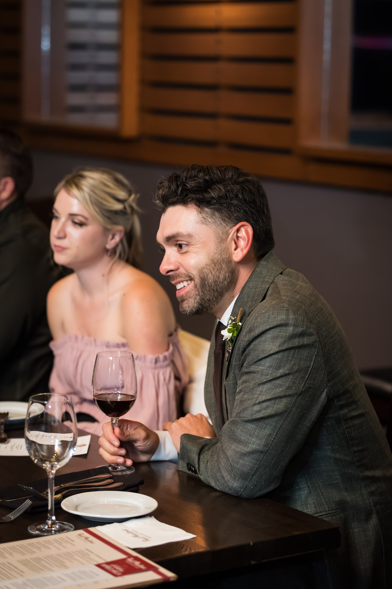 Man wearing blazer seated next to woman wearing pink dress at wedding reception