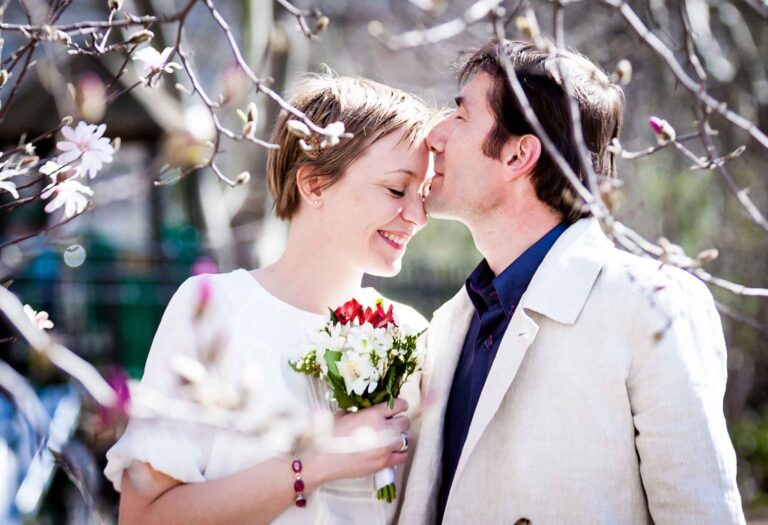 Groom kissing bride on the forehead behind flowering tree branches for article on how to elope in San Antonio