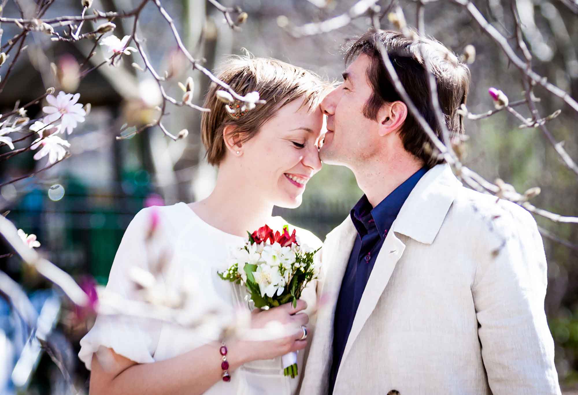 Groom kissing bride on the forehead behind flowering tree branches for article on how to elope in San Antonio