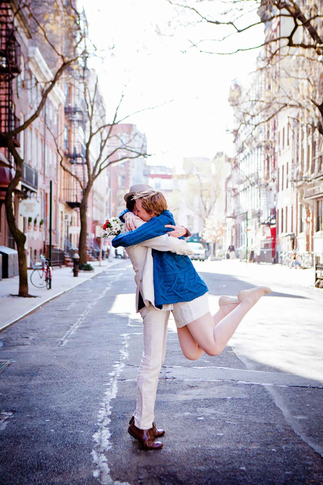 Groom hugging bride wearing blue sweater and short white dress off the ground for article on how to elope in San Antonio