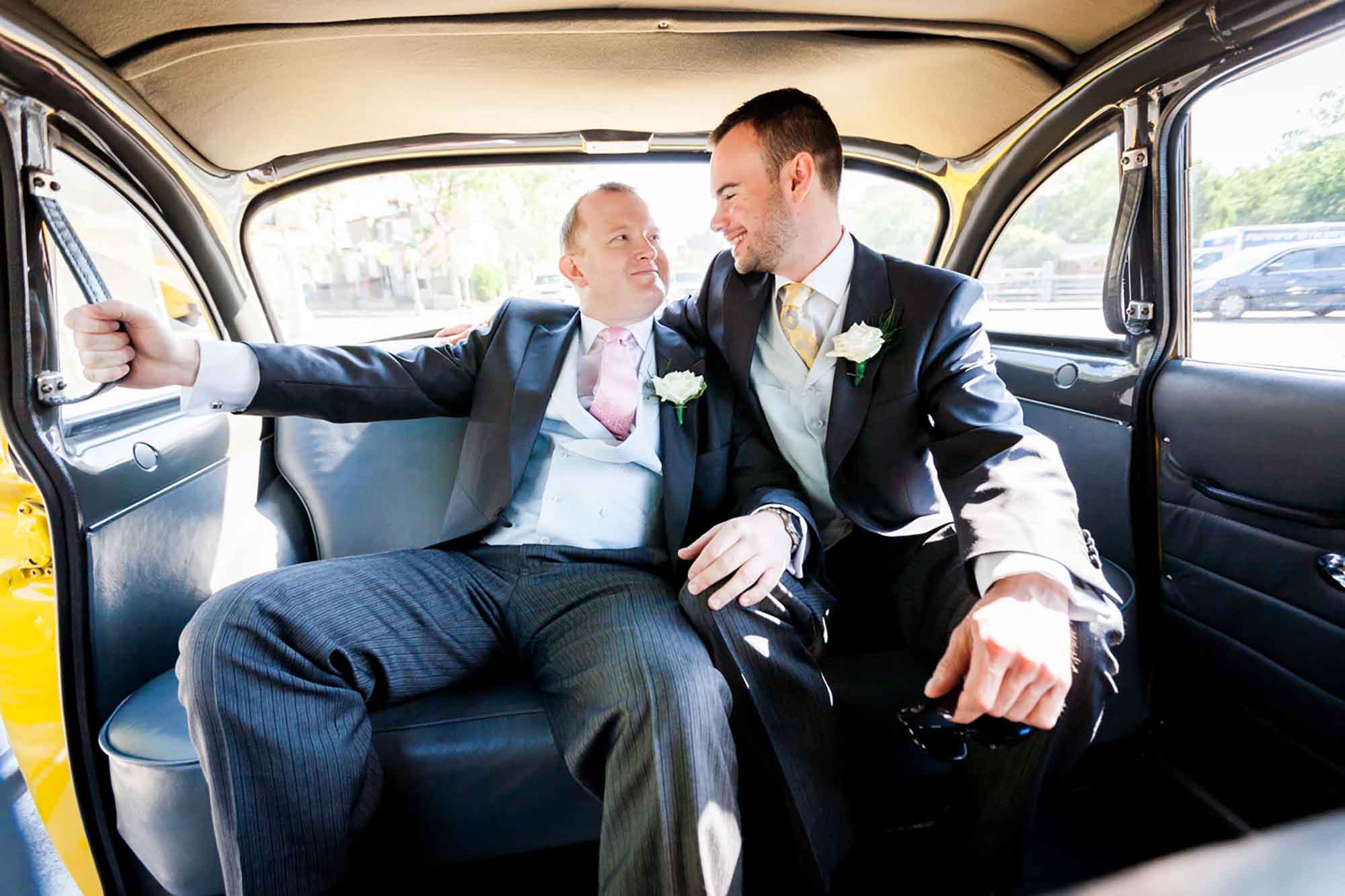 Two groom's wearing three-piece suits in the back of a yellow cab for article on how to elope in San Antonio