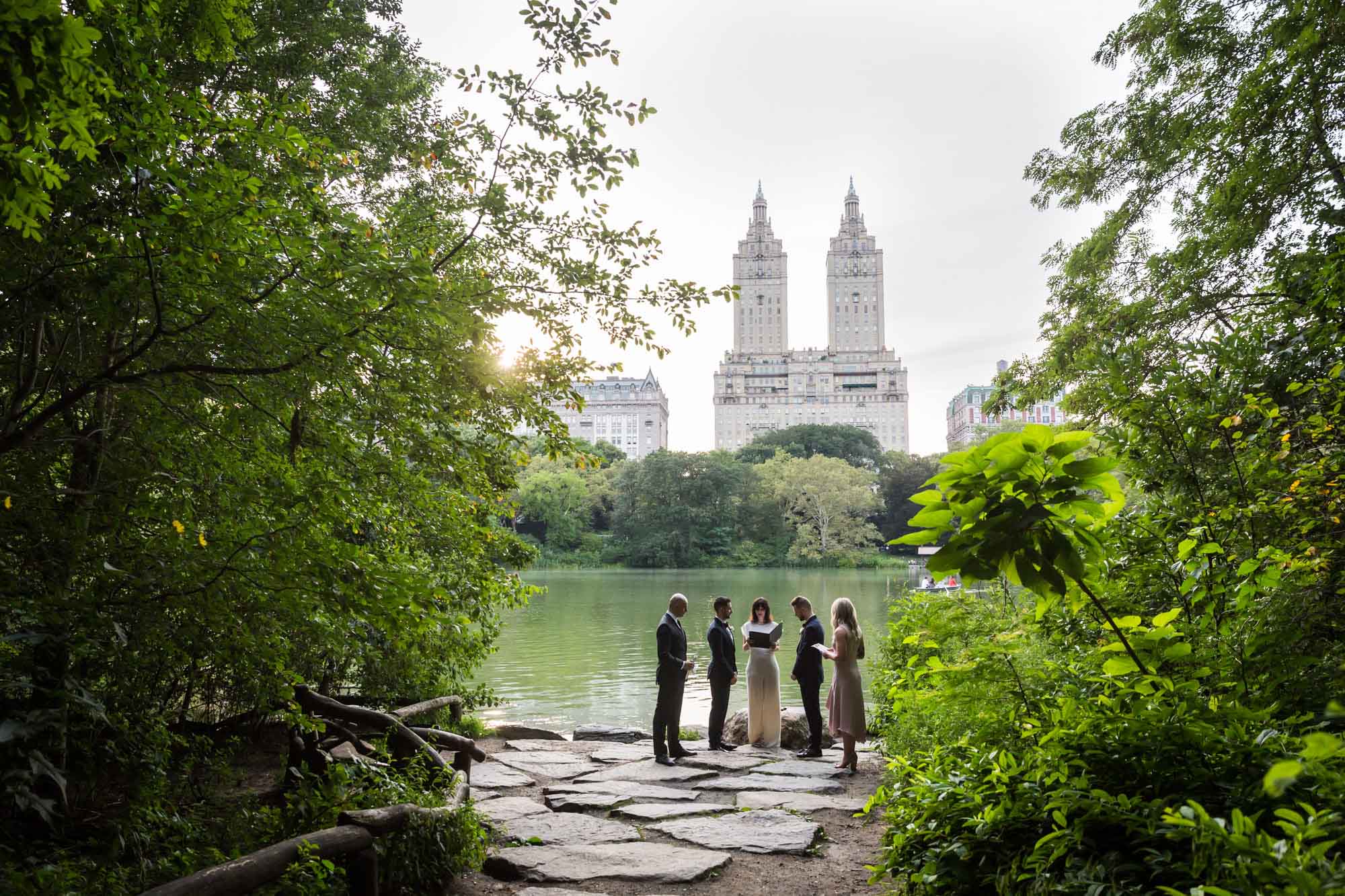 Wedding ceremony for two grooms and two witnesses on a pond in Central Park with buildings in the background for article on how to elope in San Antonio