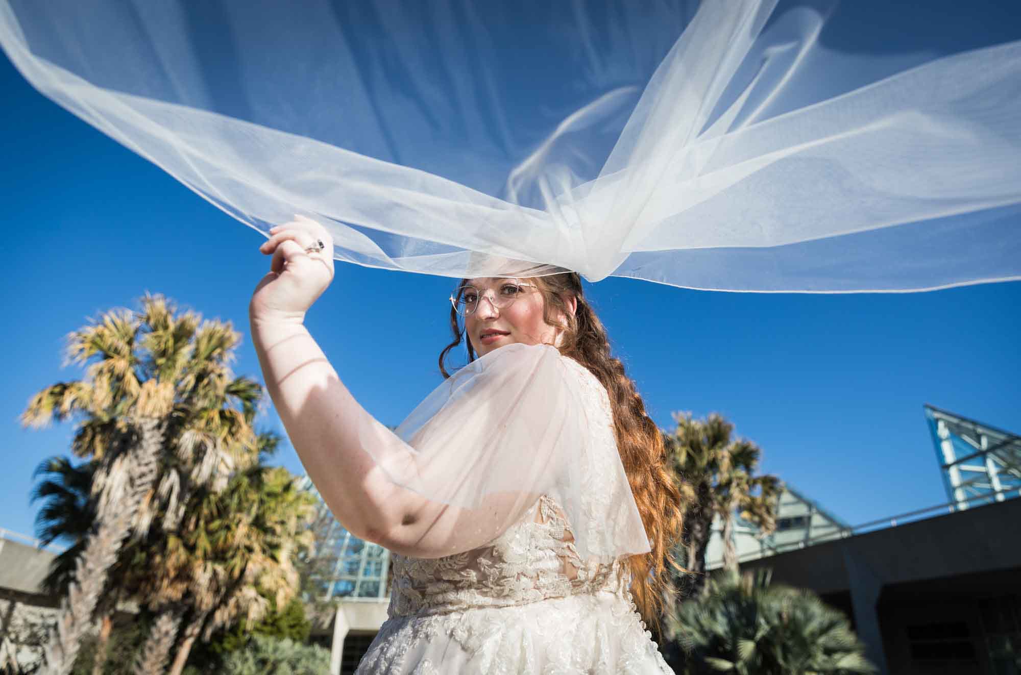 Bride wearing white dress with veil flying behind her and camera view from underneath during a San Antonio Botanical Gardens bridal portrait session