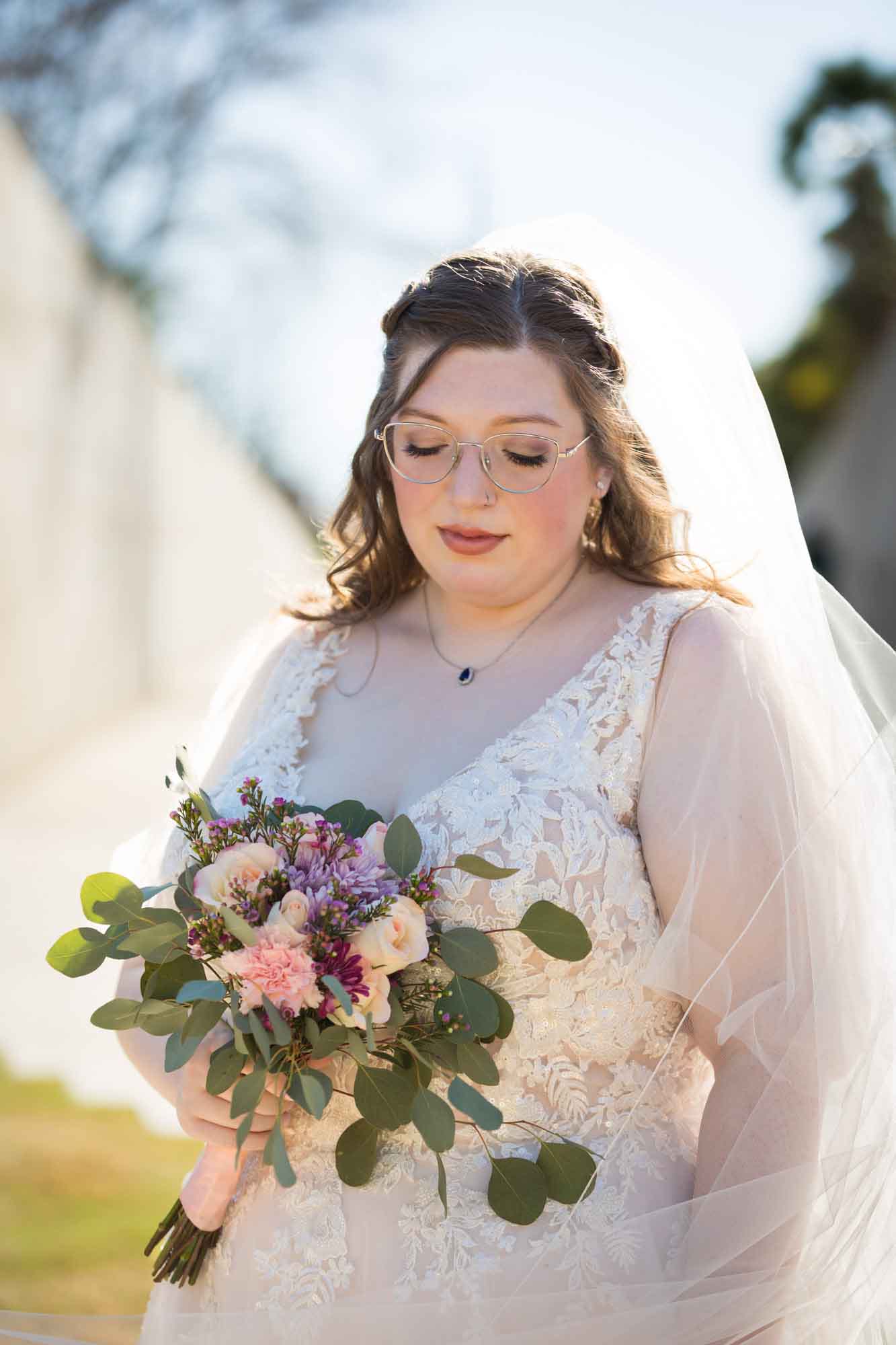 Bride wearing white dress wrapped in veil holding bouquet of flowers during a San Antonio Botanical Gardens bridal portrait session