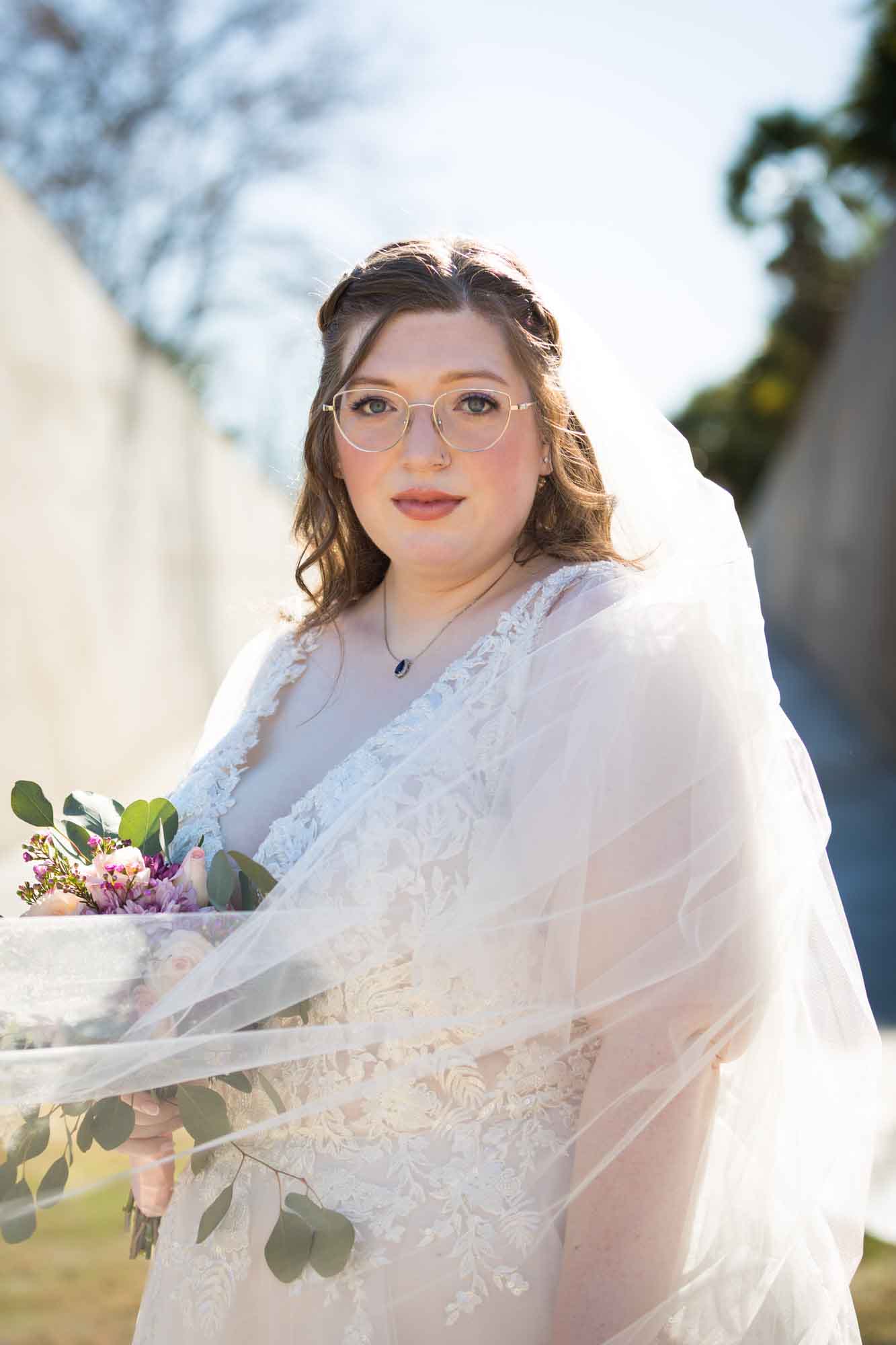 Bride wearing white dress wrapped in veil holding bouquet of flowers during a San Antonio Botanical Gardens bridal portrait session