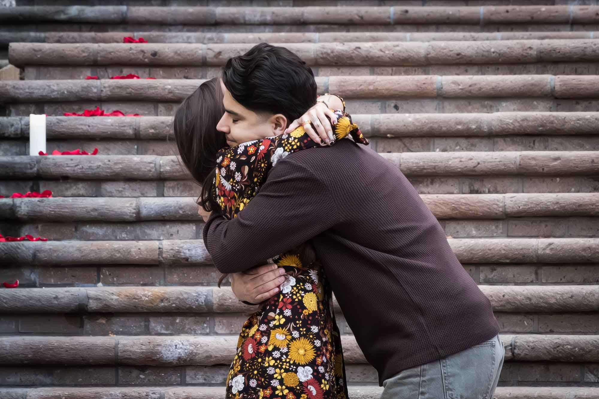 Man hugging woman in front of the stairs of the Weston Centre during a downtown San Antonio surprise proposal