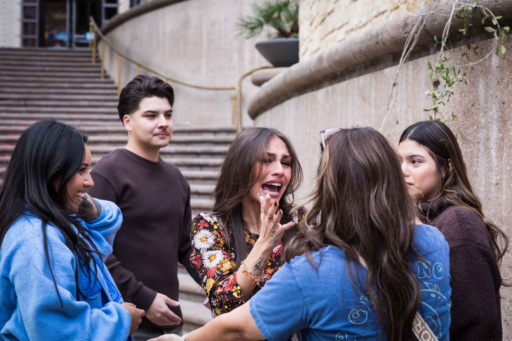 Man and four women laughing and crying in front of stairs during a downtown San Antonio surprise proposal