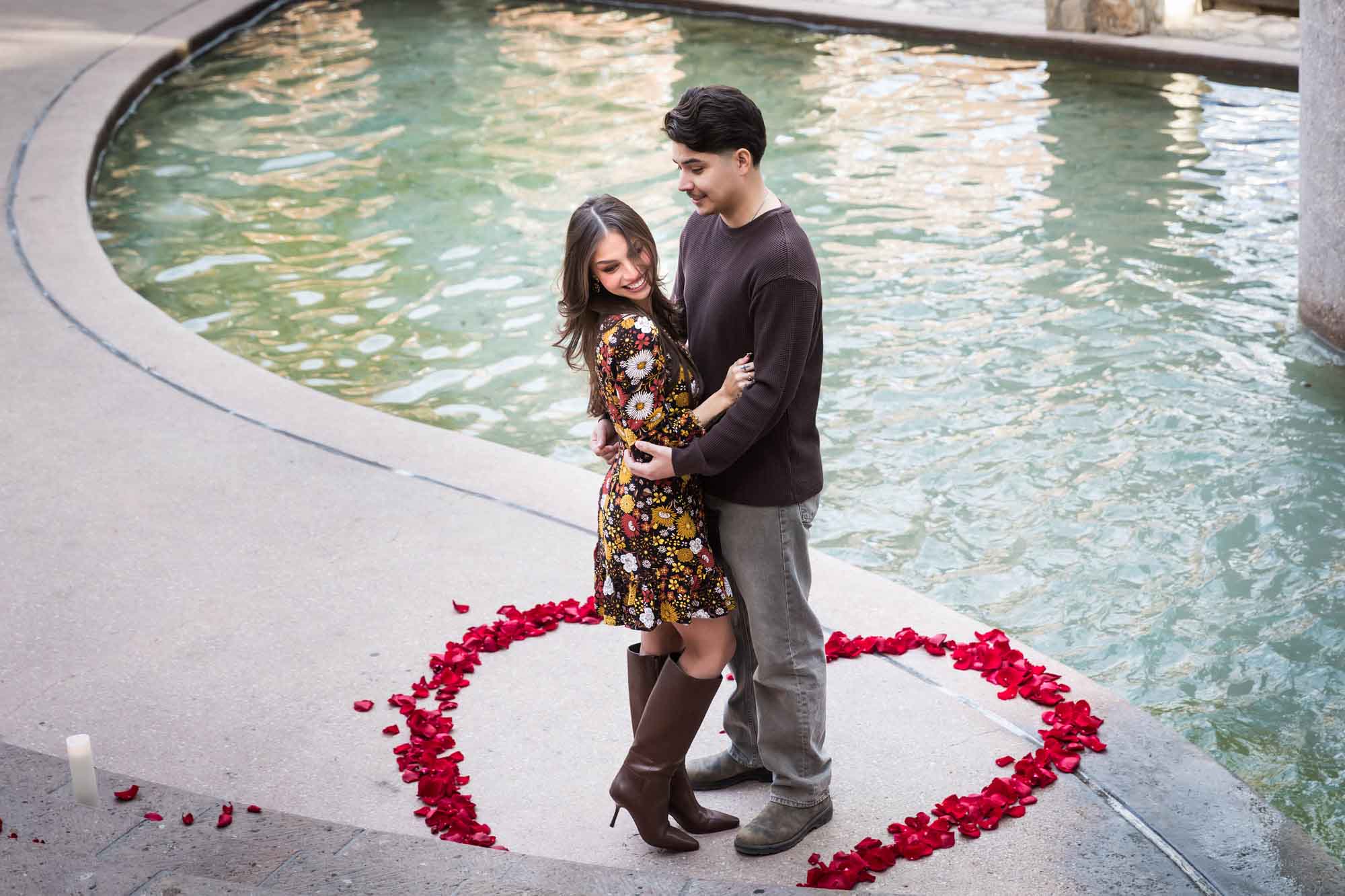 Couple hugging in middle of heart-shaped ring of rose petals during a downtown San Antonio surprise proposal