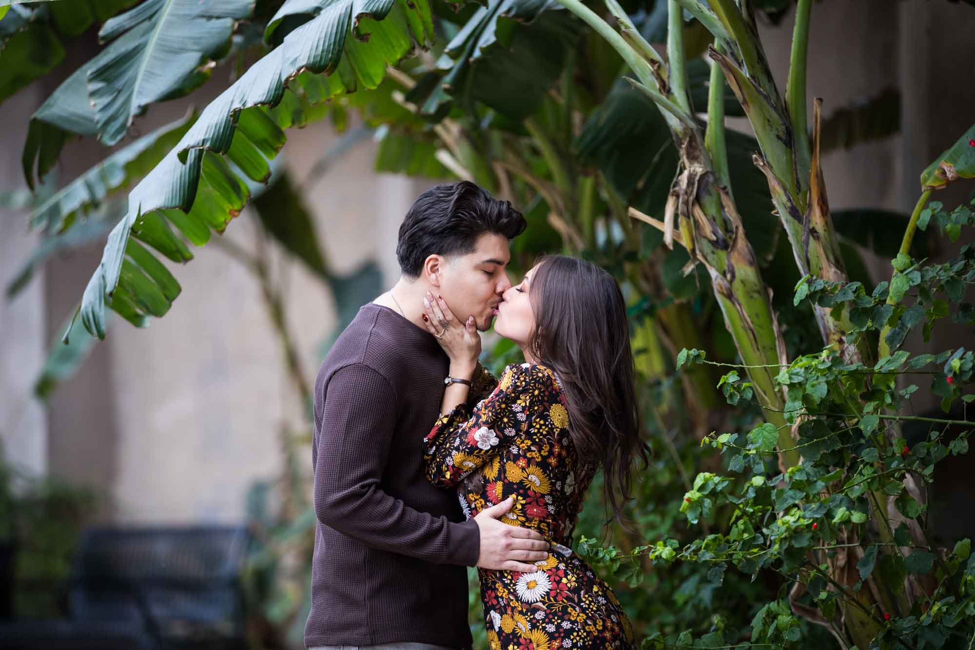 Man and woman kissing in lush landscaping of River Walk during a downtown San Antonio surprise proposal