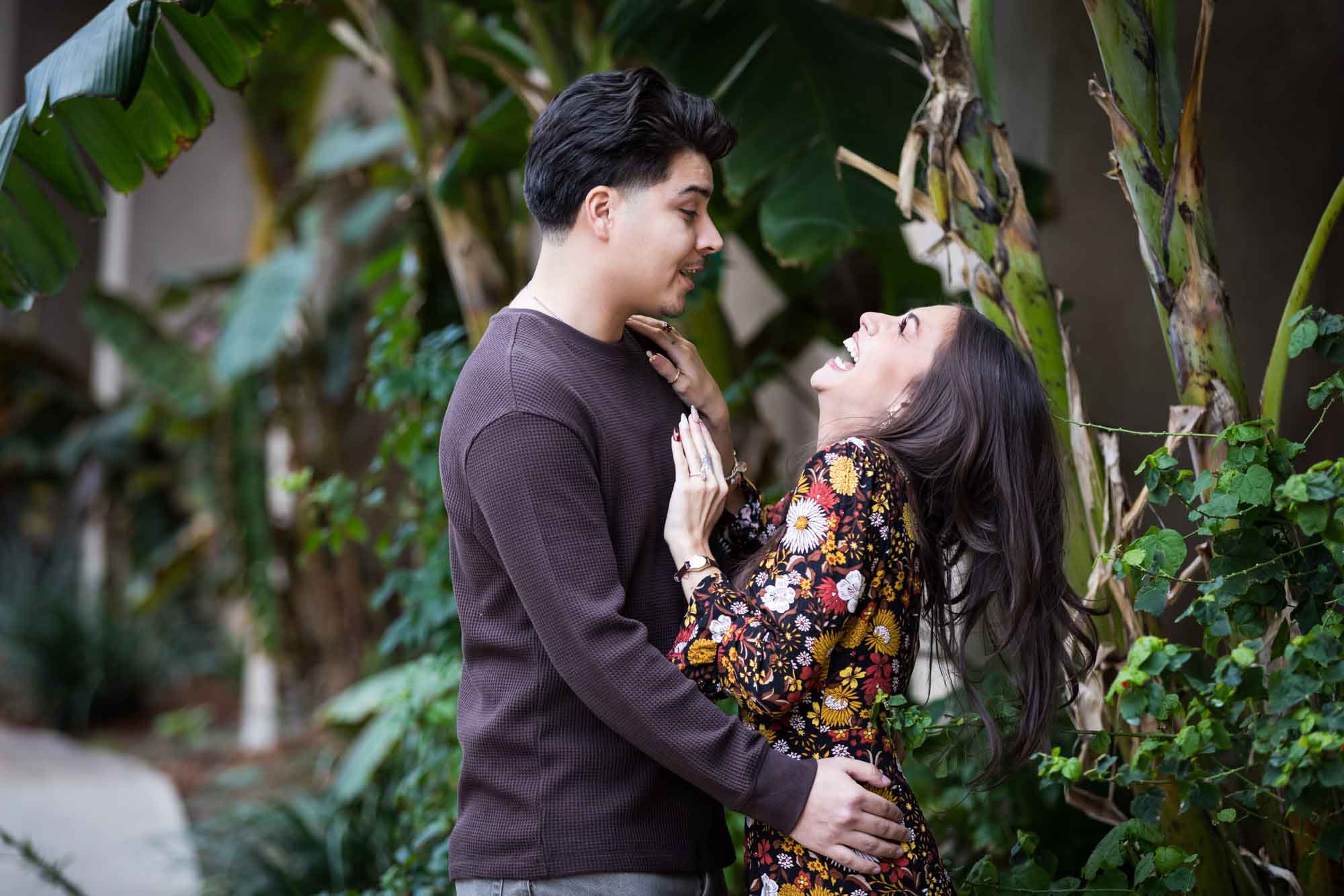Man and woman laughing in lush landscaping of River Walk during a downtown San Antonio surprise proposal