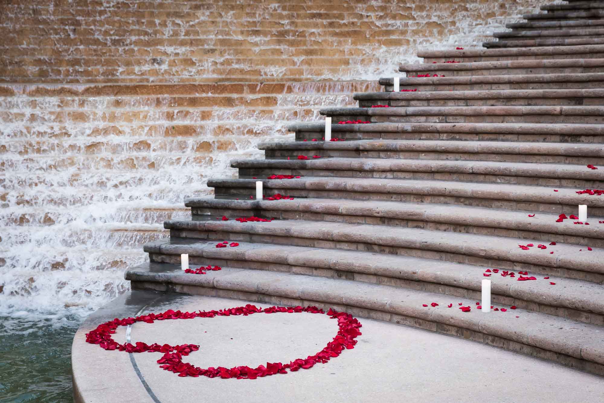 Candles on the stairs and a heart-shaped ring of rose petals in preparation for a downtown San Antonio surprise proposal at the Weston Centre