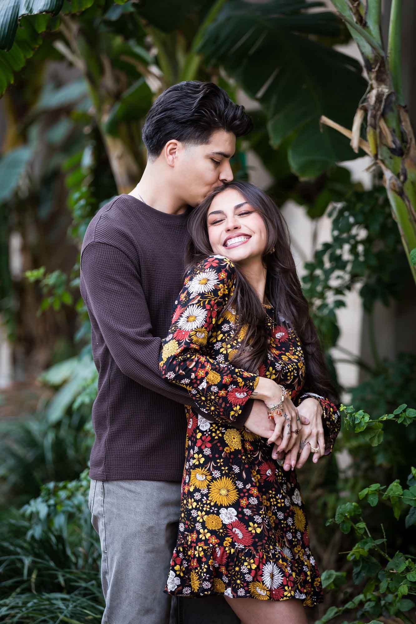 Man kissing woman on head in lush landscaping of River Walk during a downtown San Antonio surprise proposal