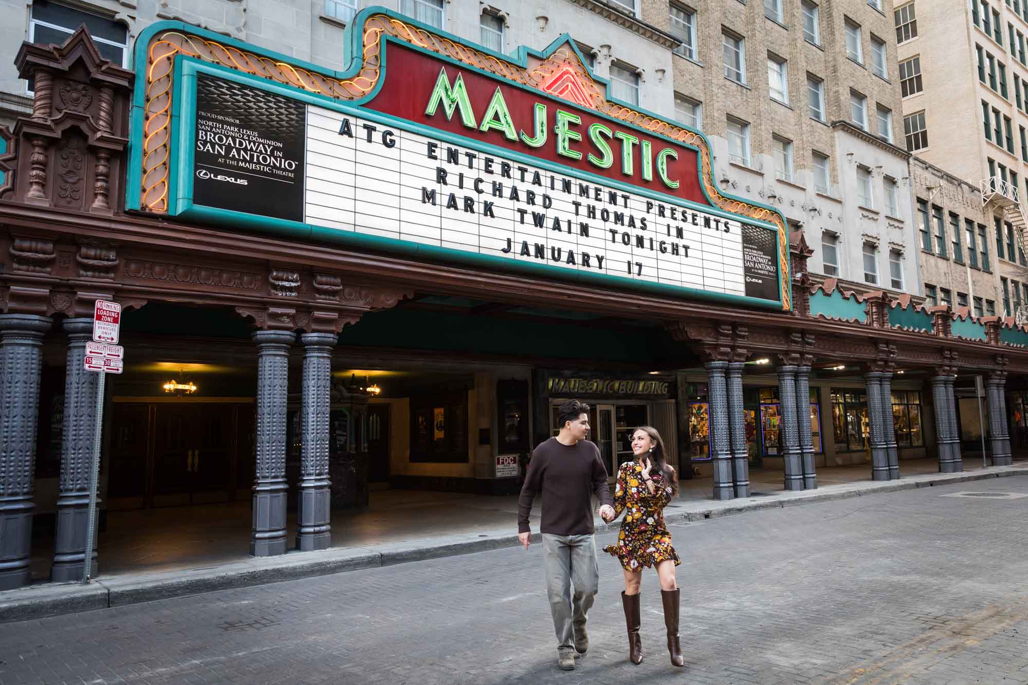 Couple holding hands walking in front of Majestic Theatre marquee in street during a downtown San Antonio surprise proposal