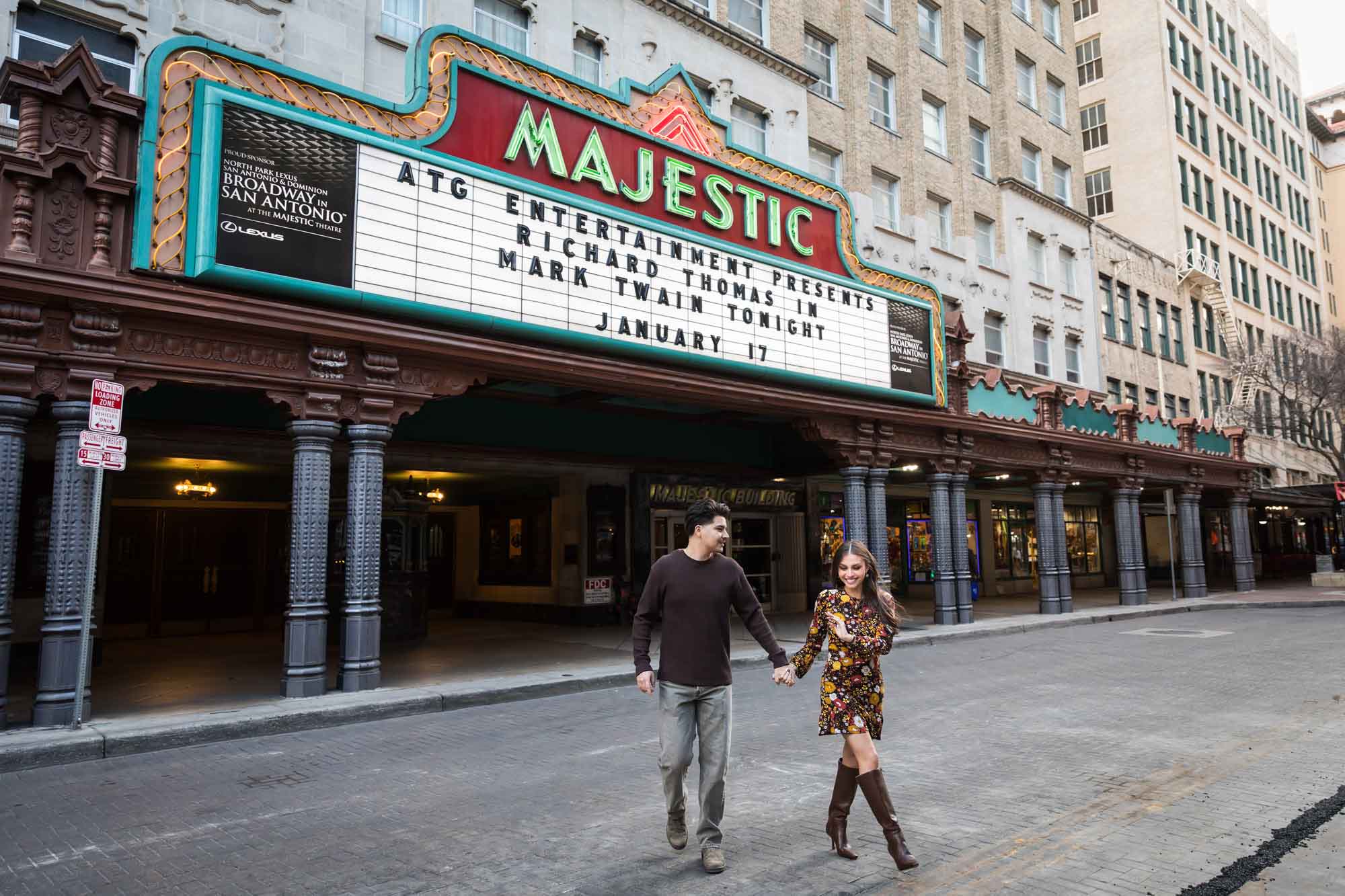 Couple holding hands walking in front of Majestic Theatre marquee in street during a downtown San Antonio surprise proposal