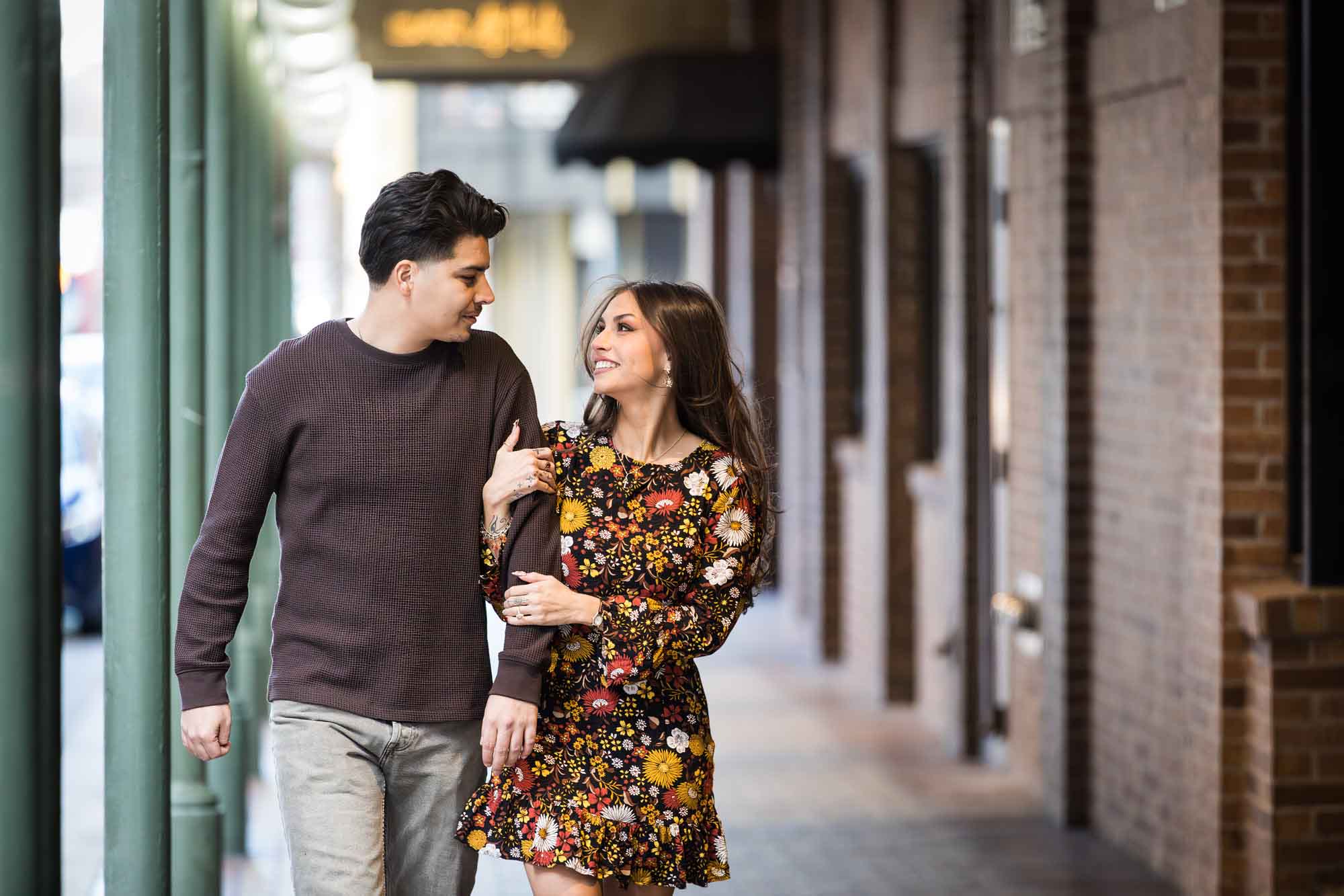 Man and woman walking arm-in-arm in front of green columns of Gunter Hotel during a downtown San Antonio surprise proposal