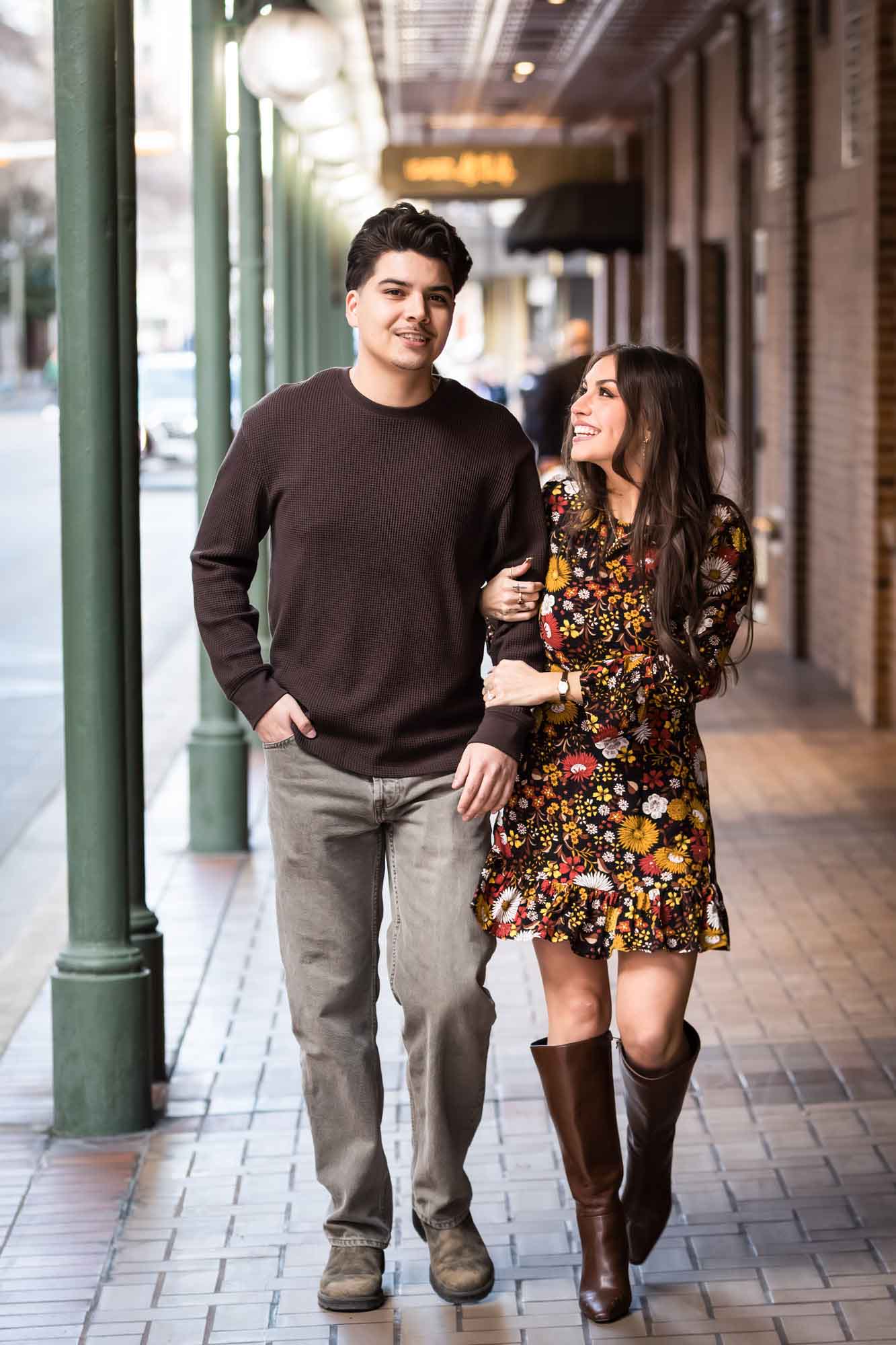 Man and woman walking arm-in-arm in front of green columns of Gunter Hotel during a downtown San Antonio surprise proposal