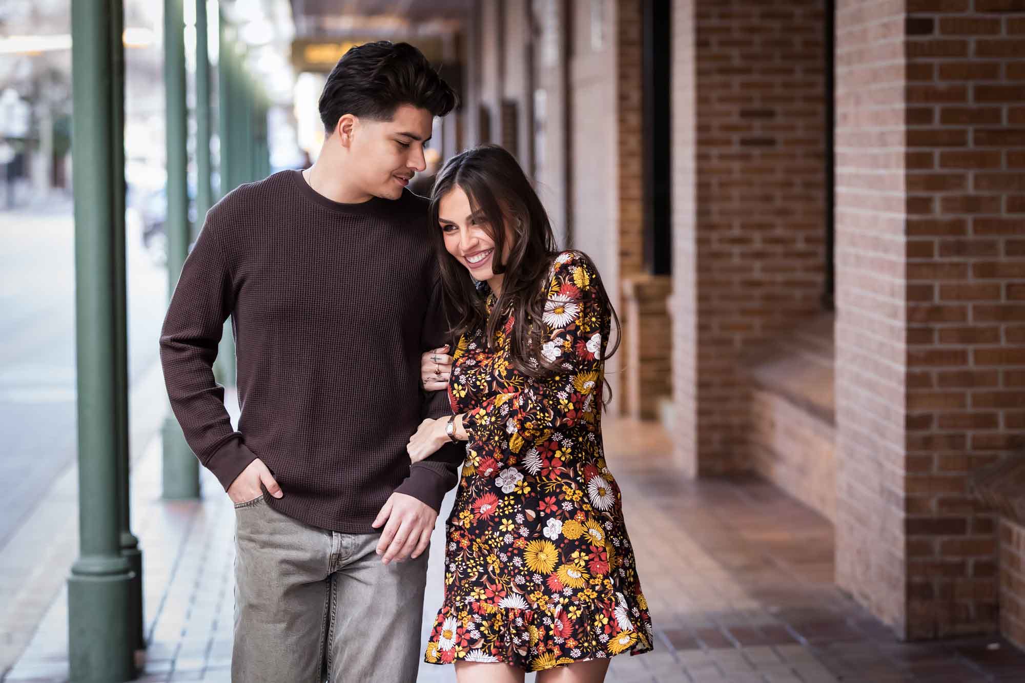 Man and woman walking arm-in-arm in front of green columns of Gunter Hotel during a downtown San Antonio surprise proposal