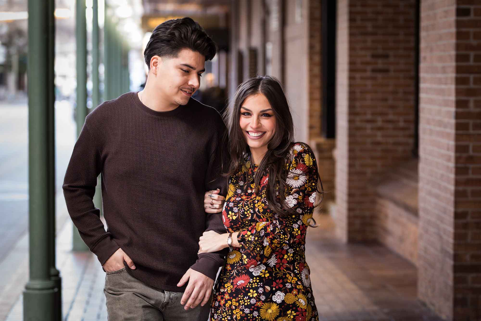 Man and woman walking arm-in-arm in front of green columns of Gunter Hotel during a downtown San Antonio surprise proposal
