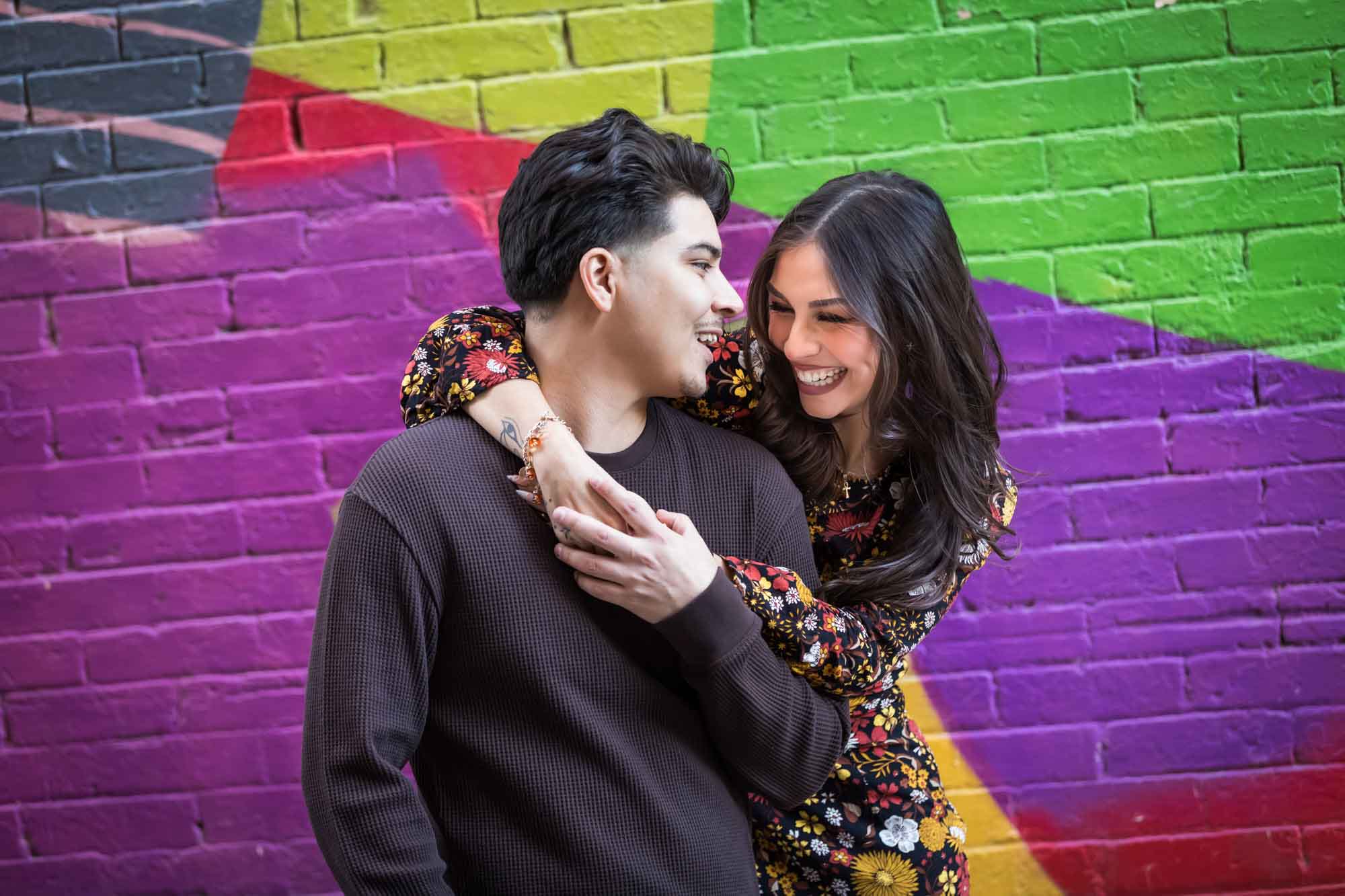 Couple looking at each other in front of colorful brick wall during a downtown San Antonio surprise proposal