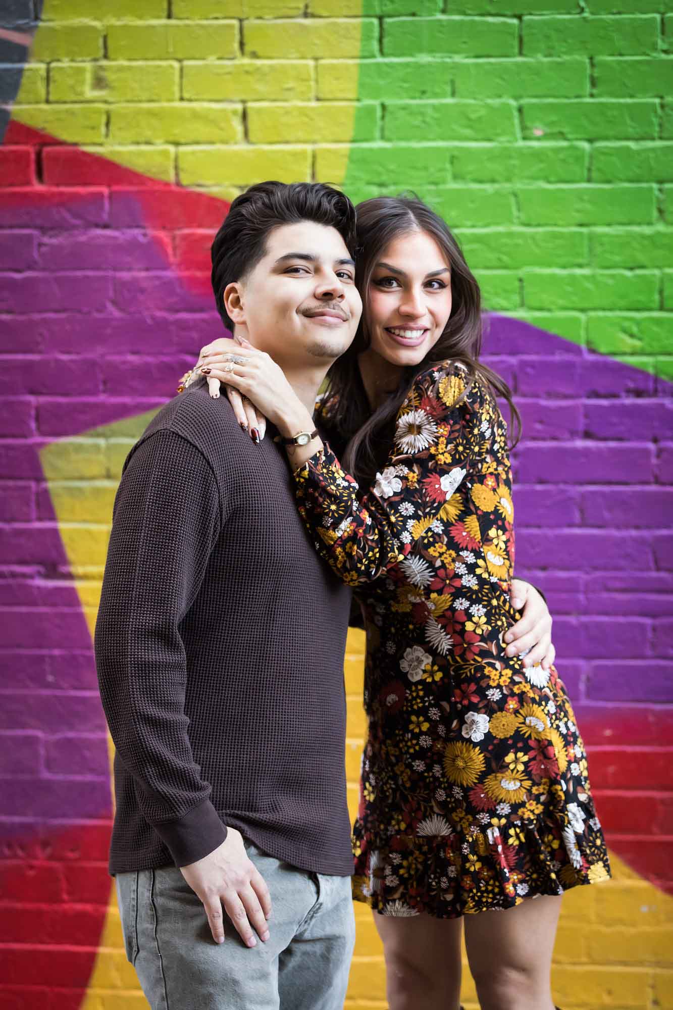 Couple hugging in front of colorful brick wall during a downtown San Antonio surprise proposal