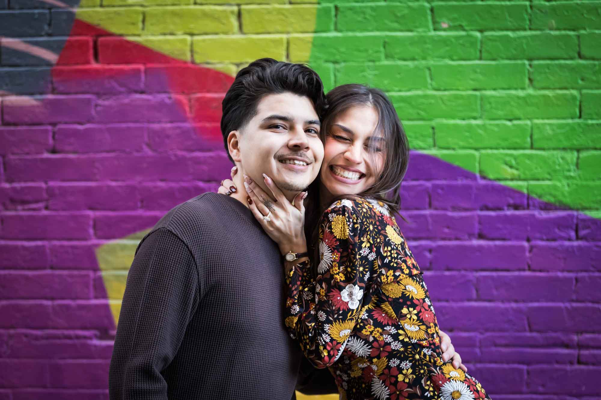 Couple hugging in front of colorful brick wall during a downtown San Antonio surprise proposal