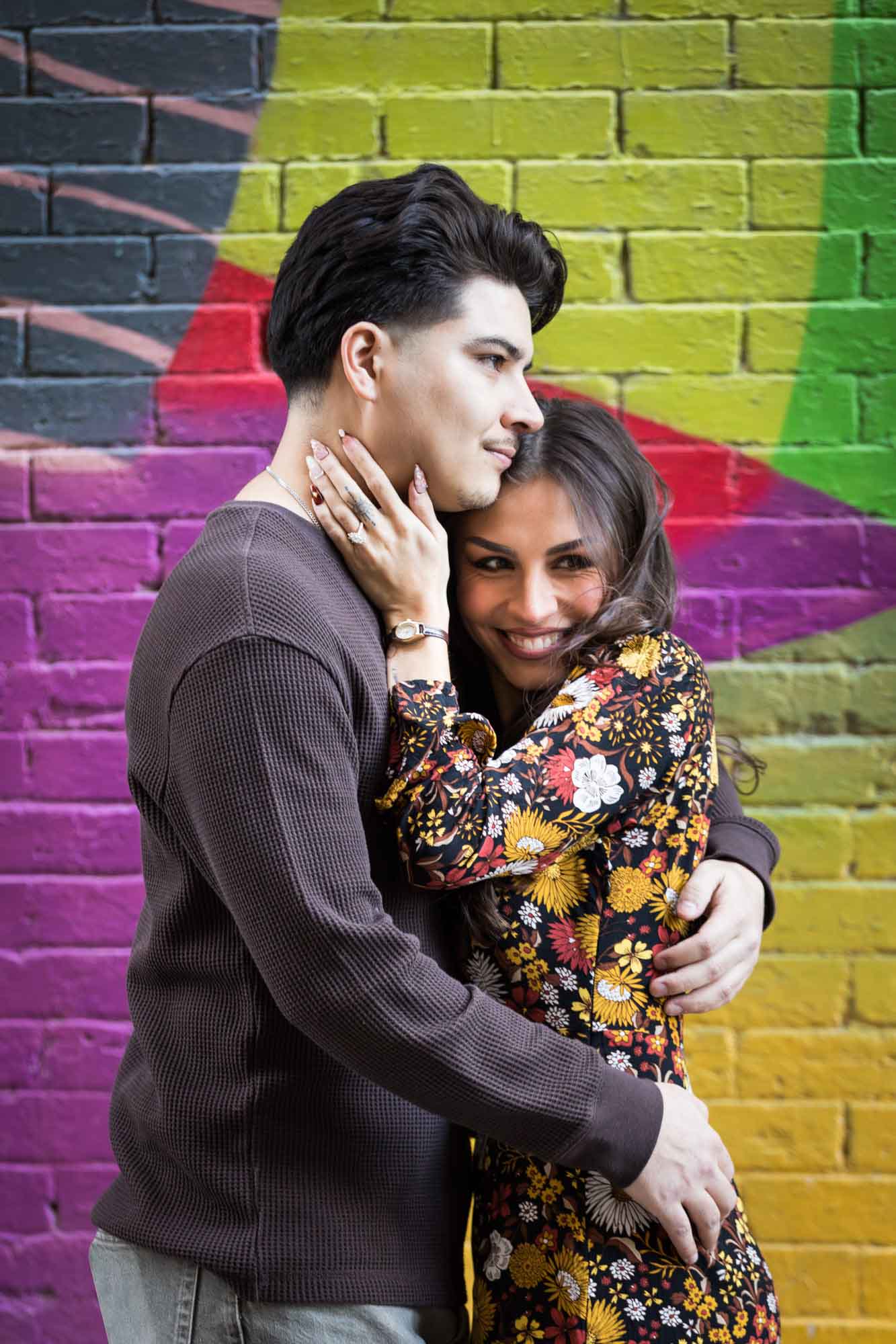 Couple hugging in front of colorful brick wall during a downtown San Antonio surprise proposal