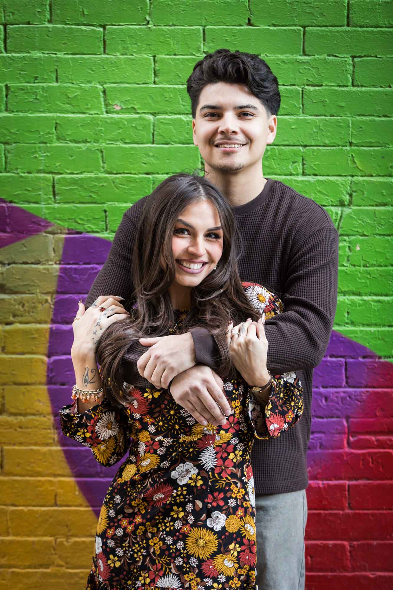 Couple hugging in front of colorful brick wall during a downtown San Antonio surprise proposal
