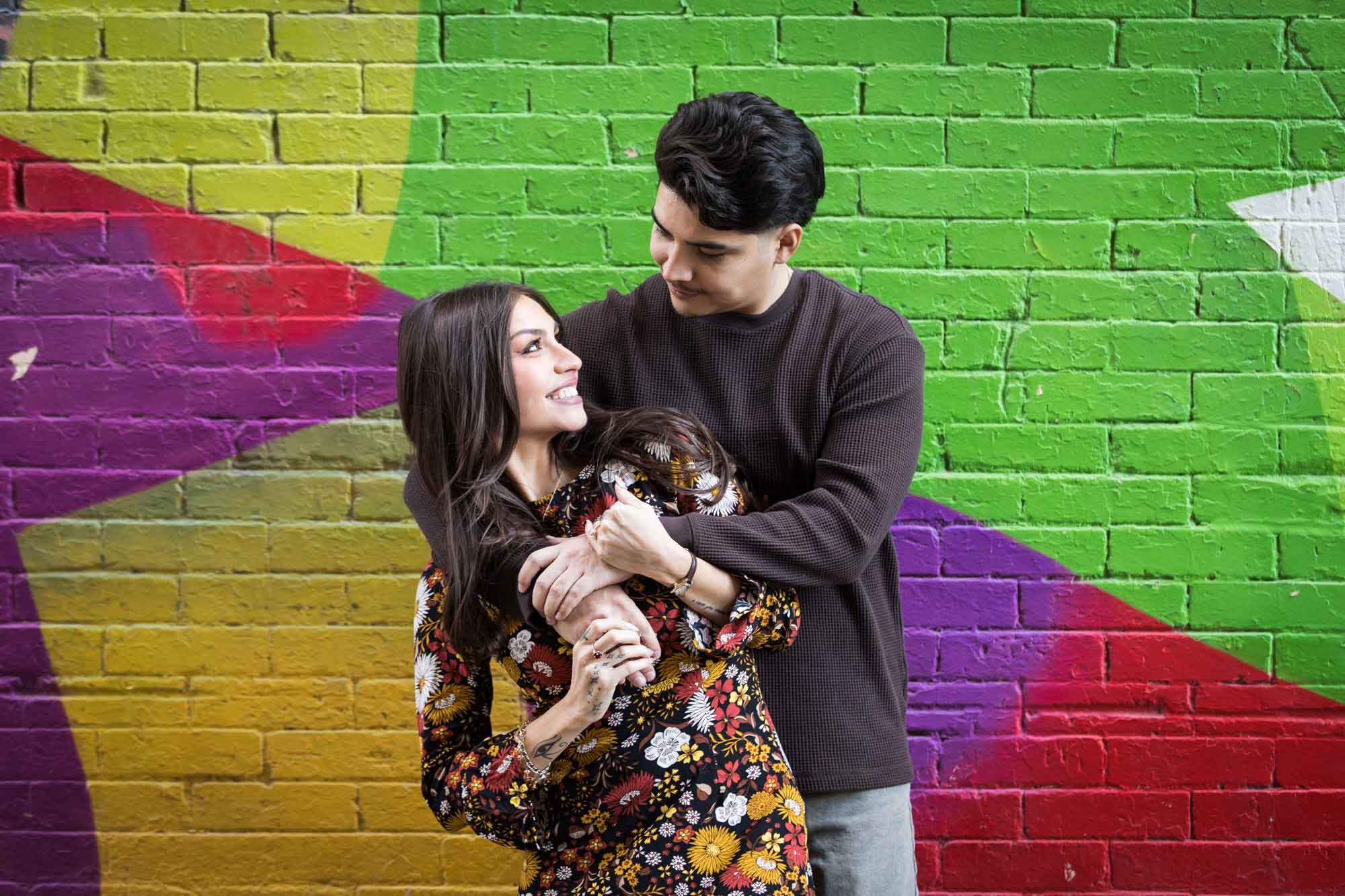 Couple hugging in front of colorful brick wall during a downtown San Antonio surprise proposal