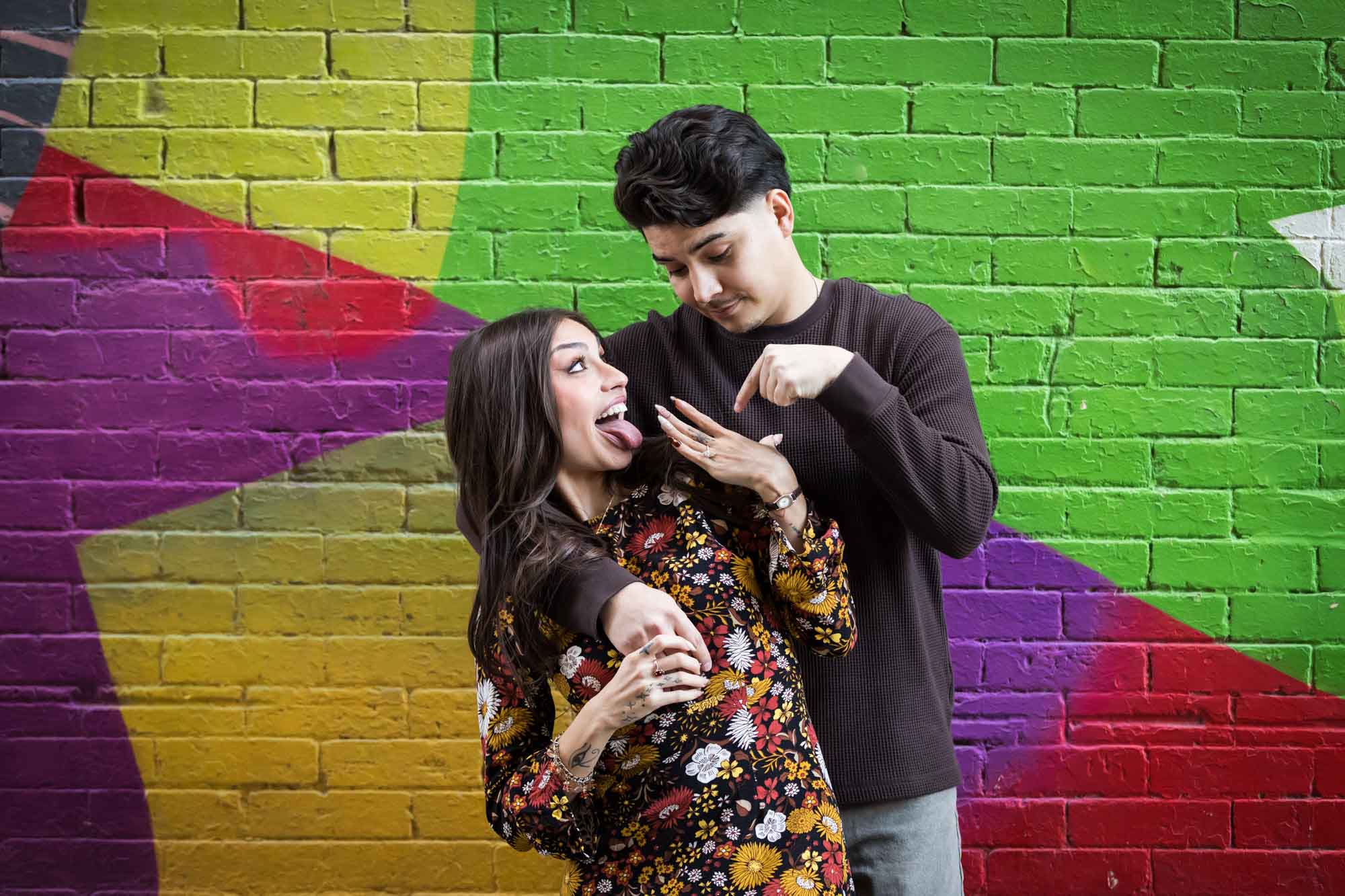 Woman showing off engagement ring to man in front of colorful brick wall during a downtown San Antonio surprise proposal