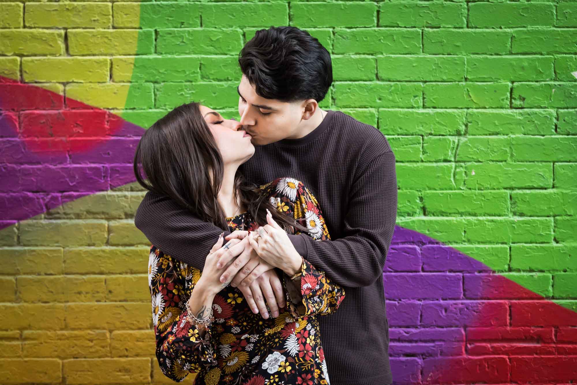 Couple kissing in front of colorful brick wall during a downtown San Antonio surprise proposal
