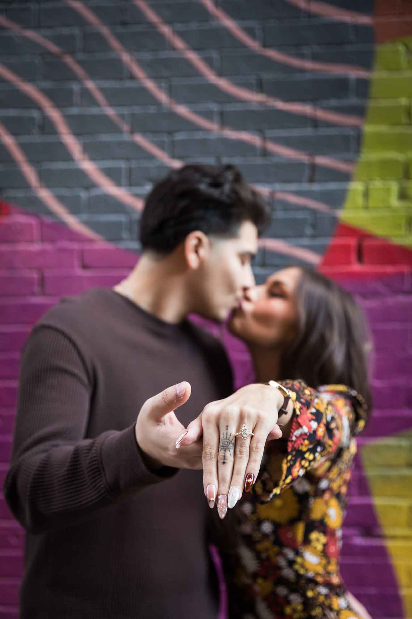 Couple showing off engagement ring on woman's hand in front of colorful brick wall during a downtown San Antonio surprise proposal