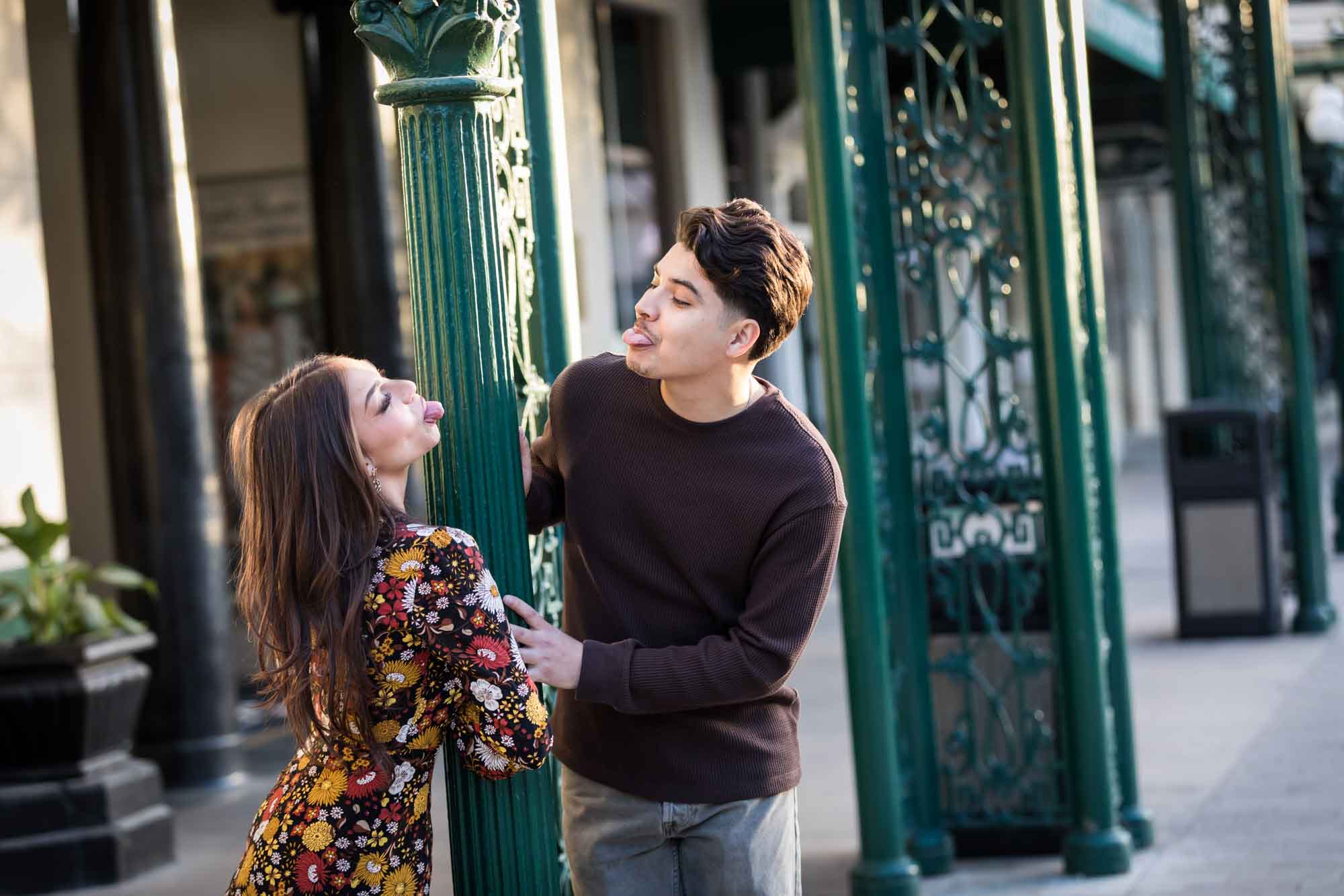 Couple sticking tongues out at each other in front of green column of Menger Hotel during a downtown San Antonio surprise proposal